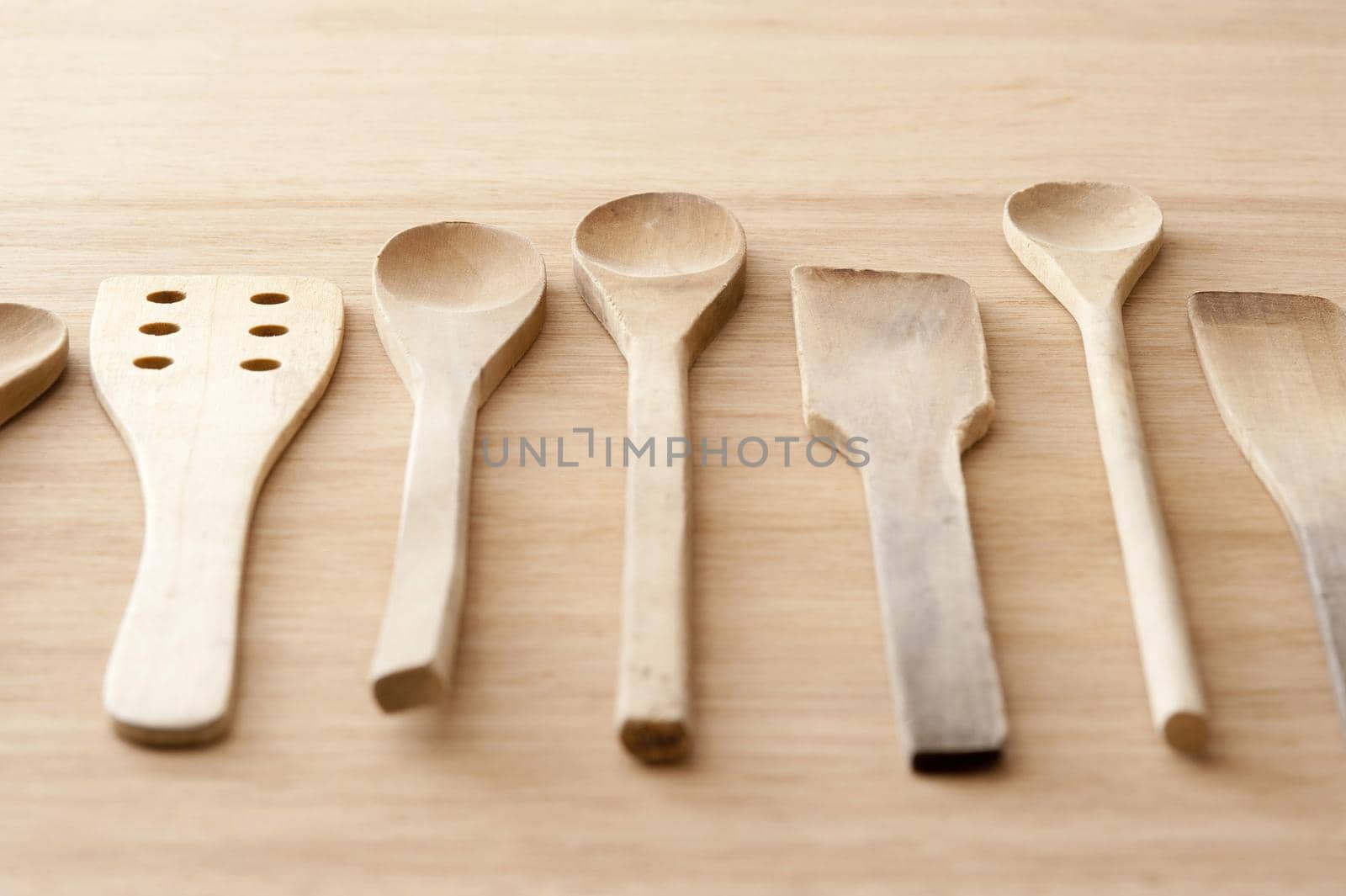 Set of different plain wooden kitchen spoons and spatulas laid out on a kitchen table in a neat row ready for cooking