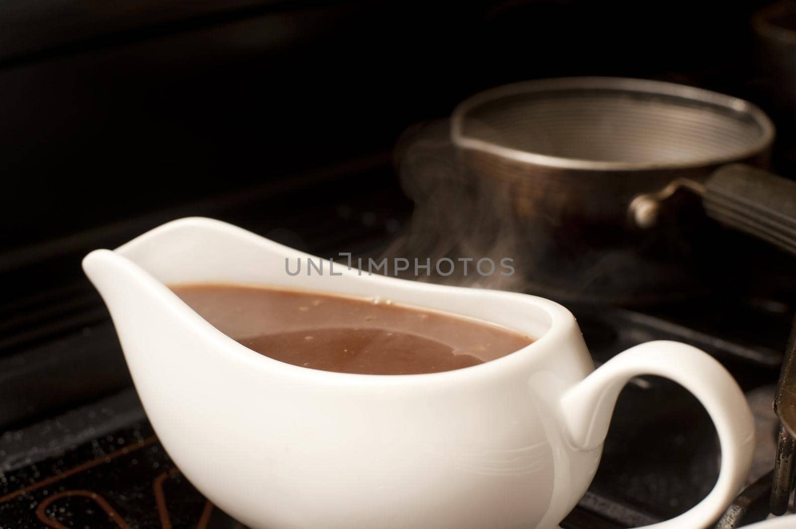 Close up view of a plain white ceramic gravy boat filled with delicious rich gravy made with the meat juices from a roast