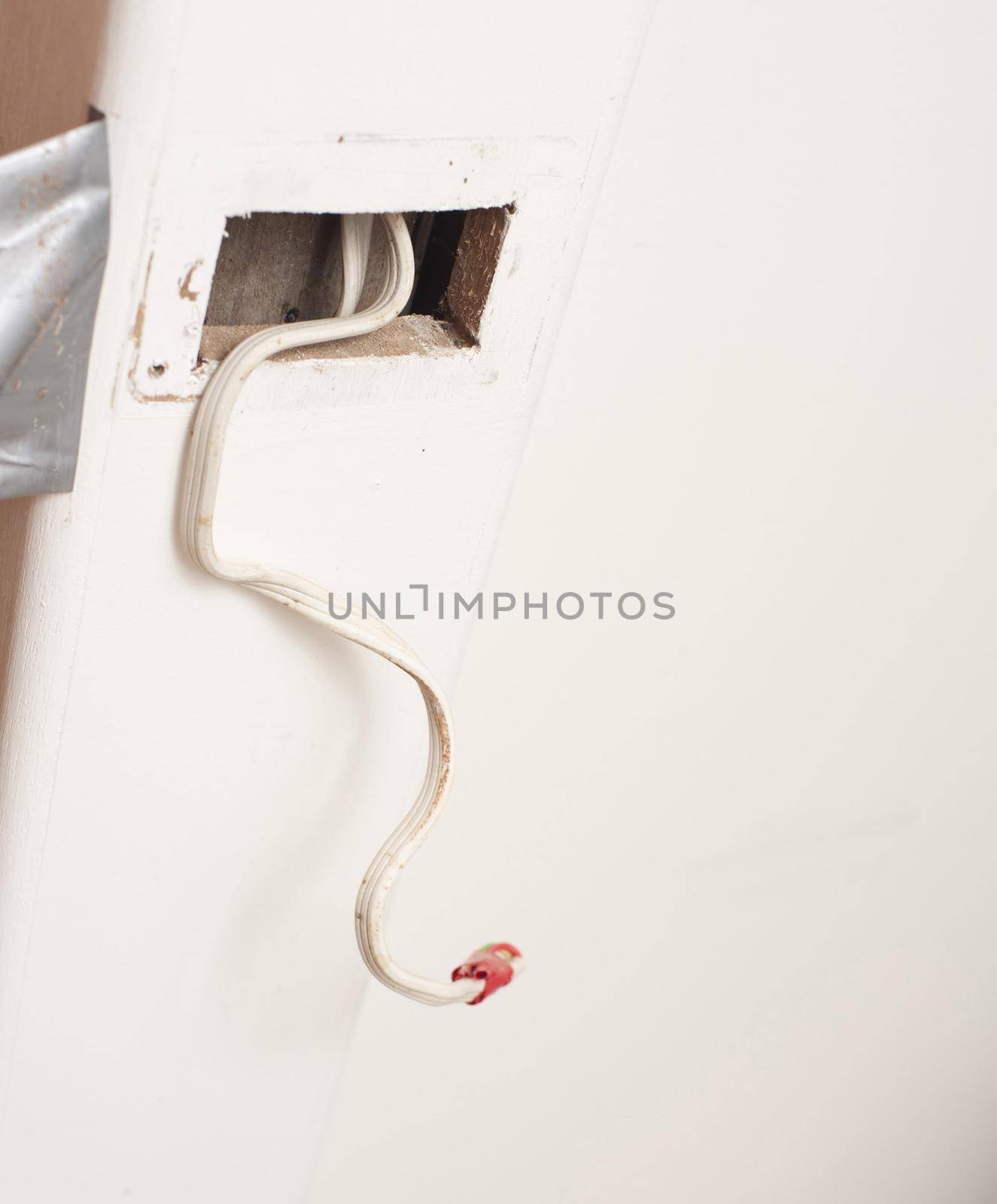 New electrical wiring being installed in a house during a renovation project with a taped off wire protruding from an access point in the wall