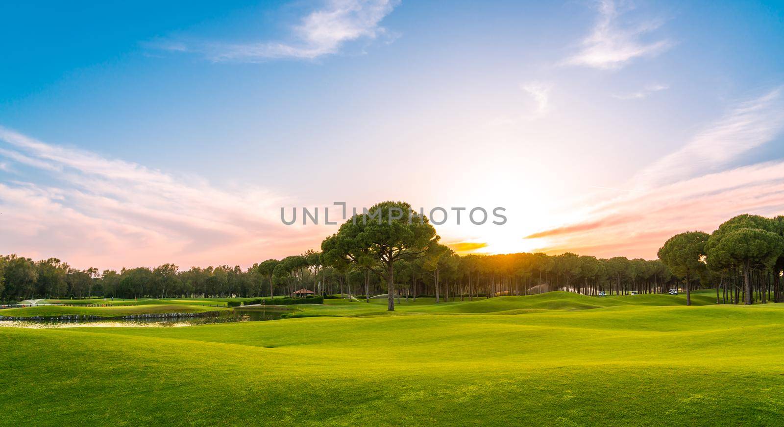 Golf course at sunset with beautiful sky. Scenic panoramic view of golf fairway