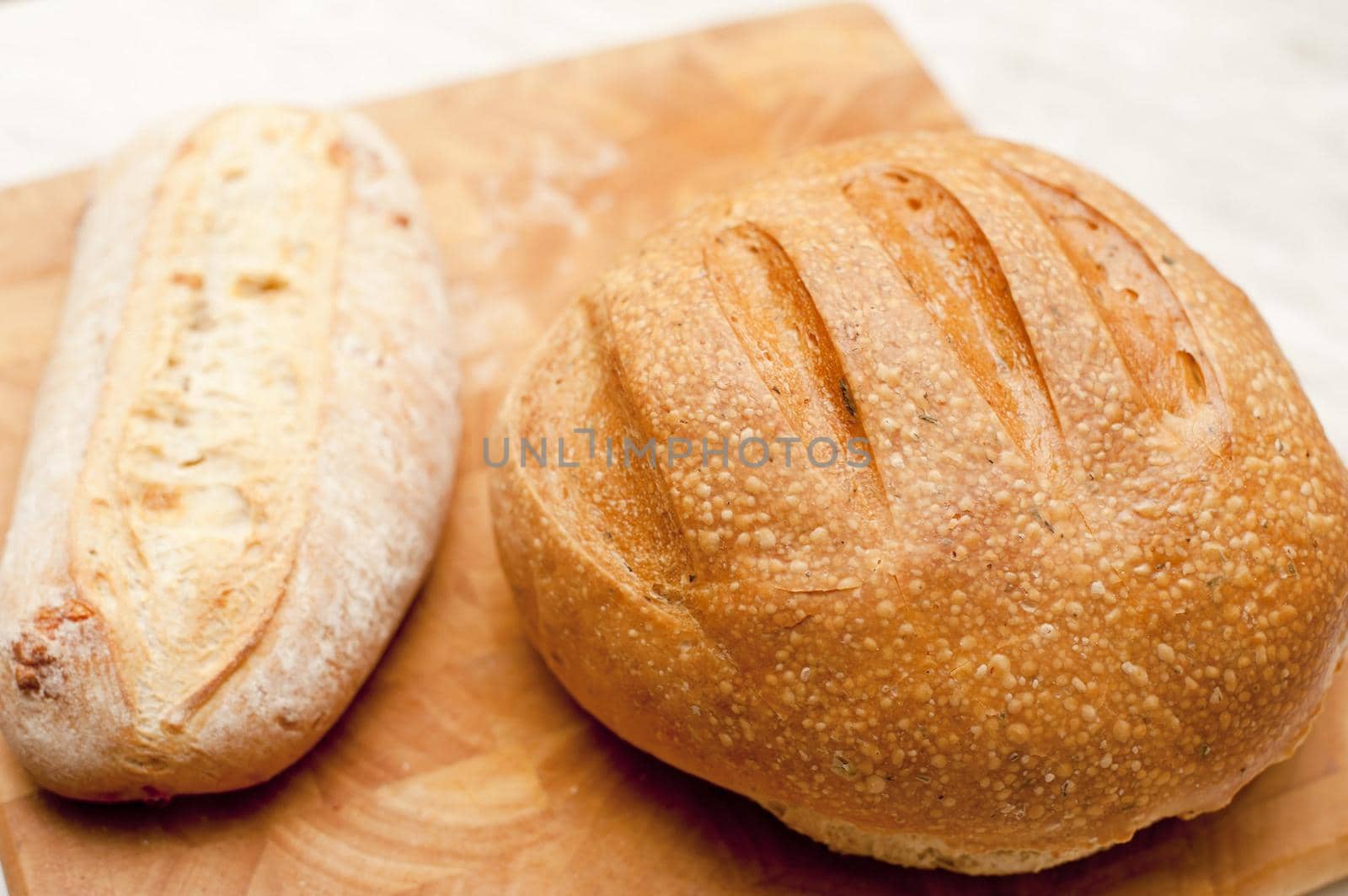 Two freshly baked uncut crusty loaves of bread, one round and one long, on a wooden bread board