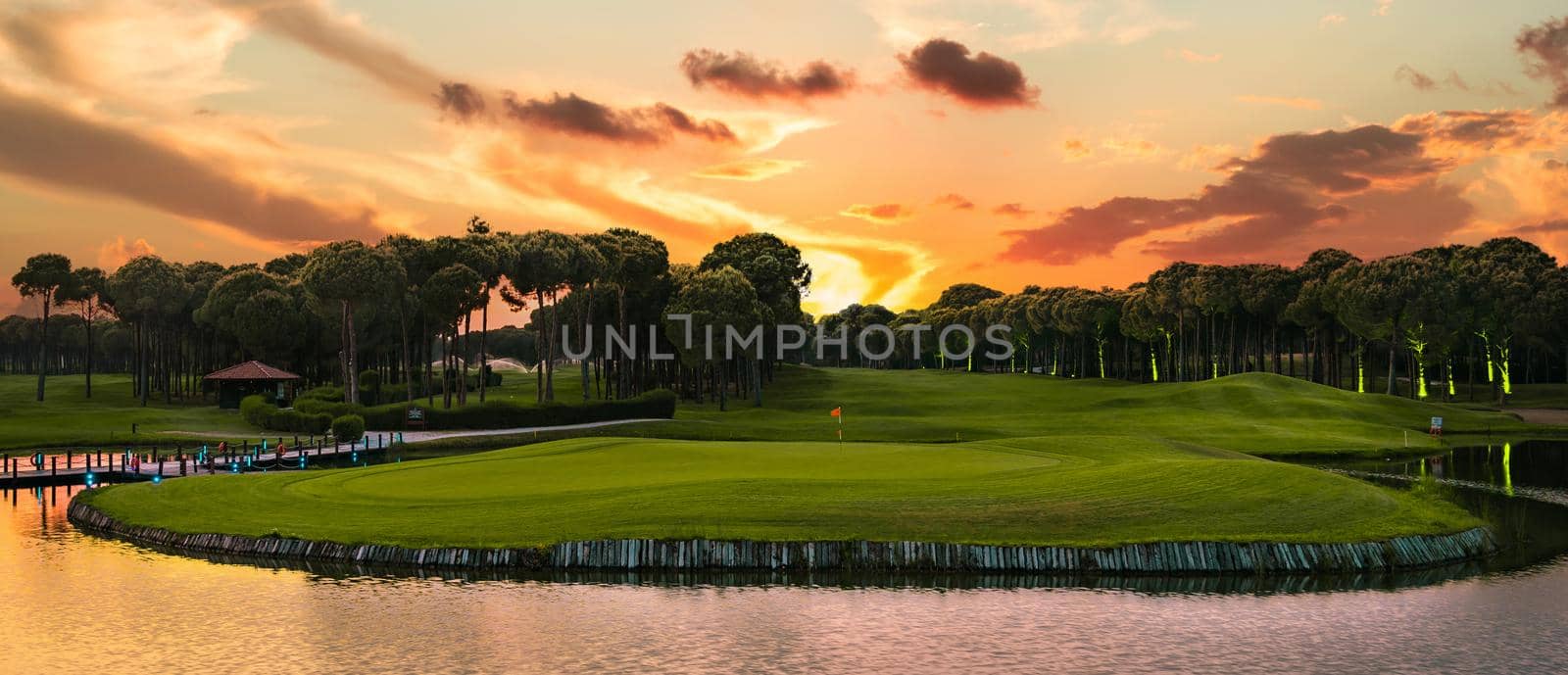 Panoramic view of beautifPanoramic view of beautiful golf course with pines at sunset. Golf field with fairway, lake and pines