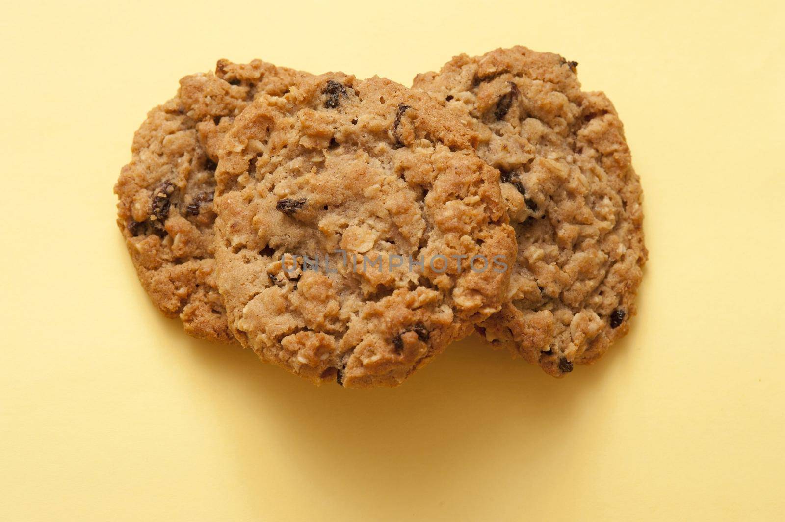 Overhead view of a pile of crunchy raisin cookies on a pale yellow background with copyspace