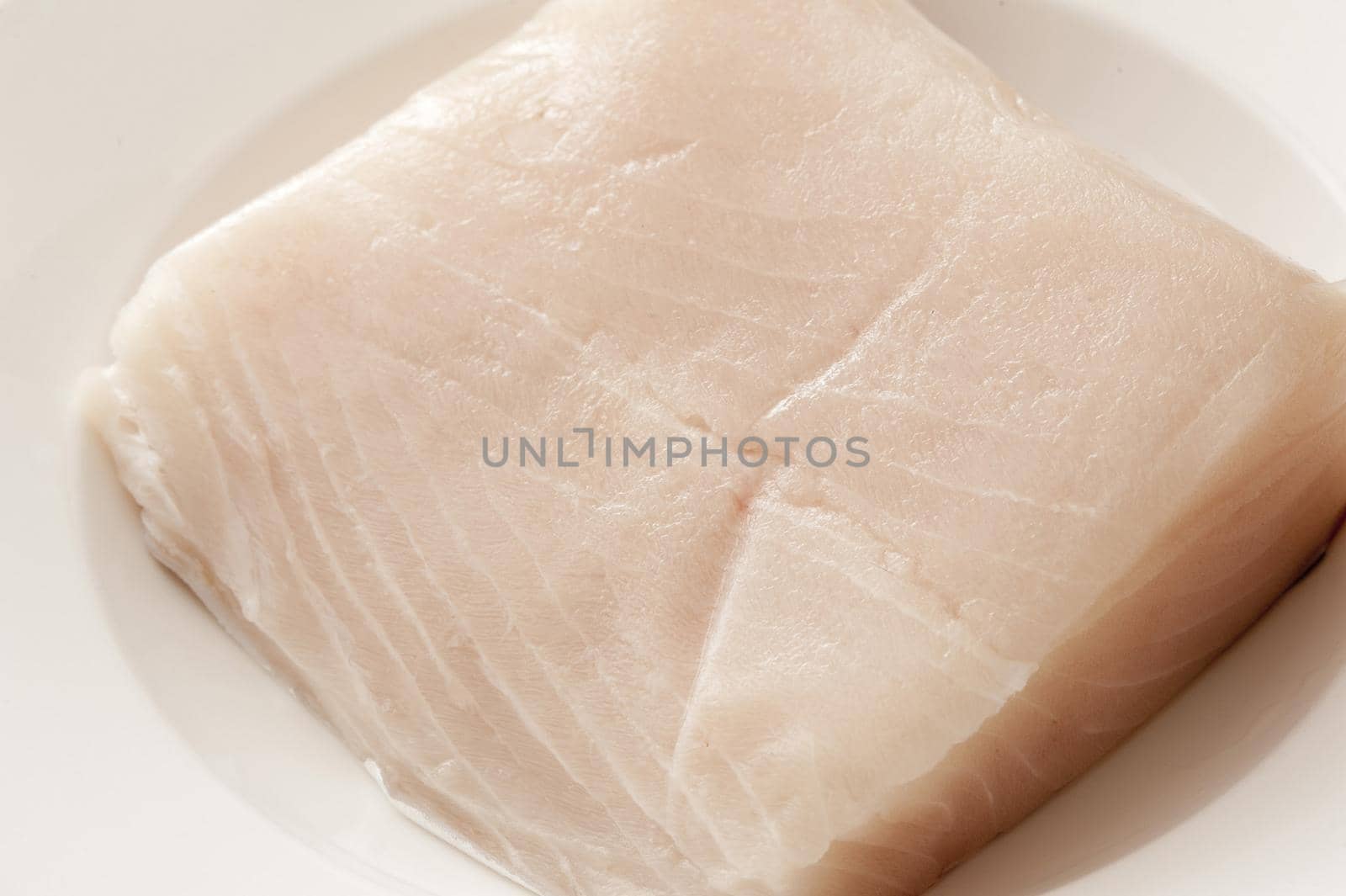 Close up on raw piece of light colored mackerel fish on white shiny plate