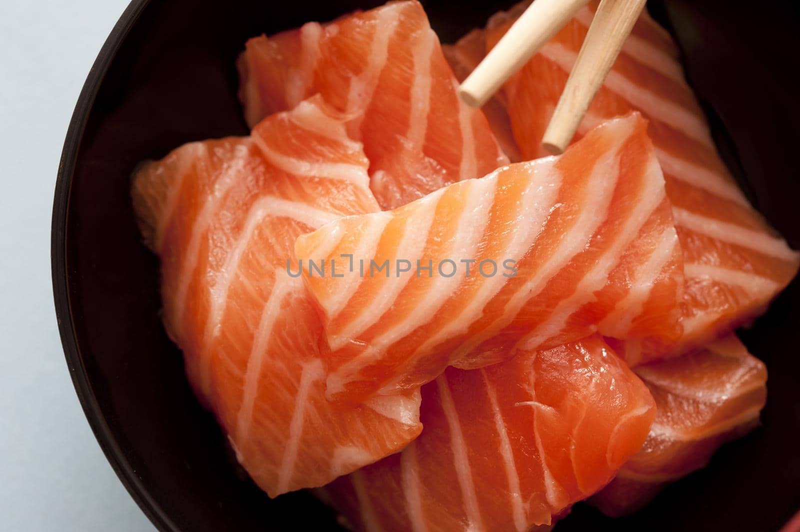 First person perspective view from top down over sashimi raw fish strips with chopsticks close up