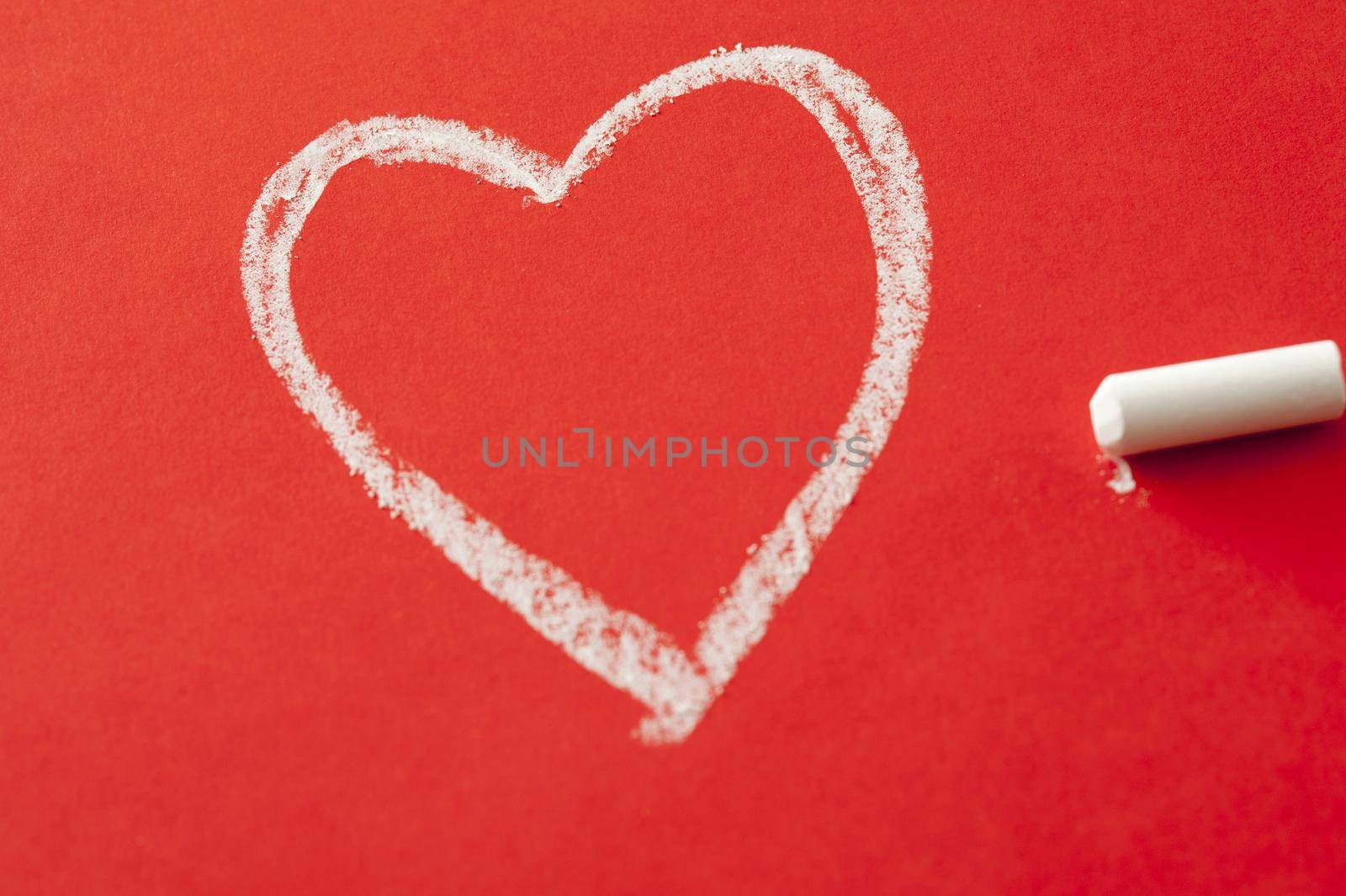 Love and romance concept with a heart shape drawn in chalk on a red background with the stick of chalk alongside
