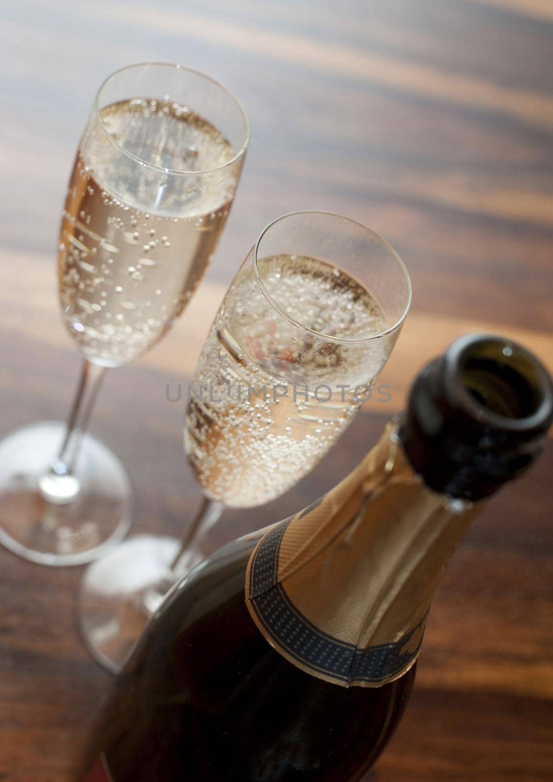 Two flutes of romantic sparkling white champagne standing alongside a champagne bottle on a wooden table ready to celebrate a special occasion, close up high angle view