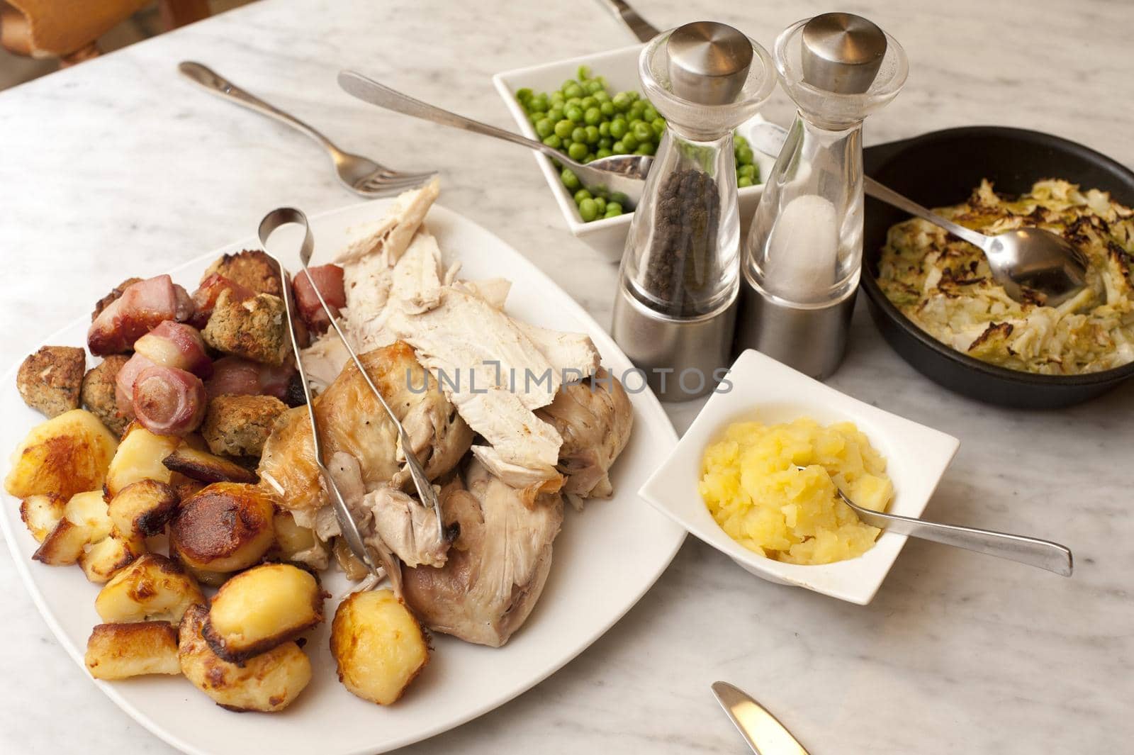 Chicken roast carved and displayed on a plate with golden roast potatoes and individual side servings of vegetables