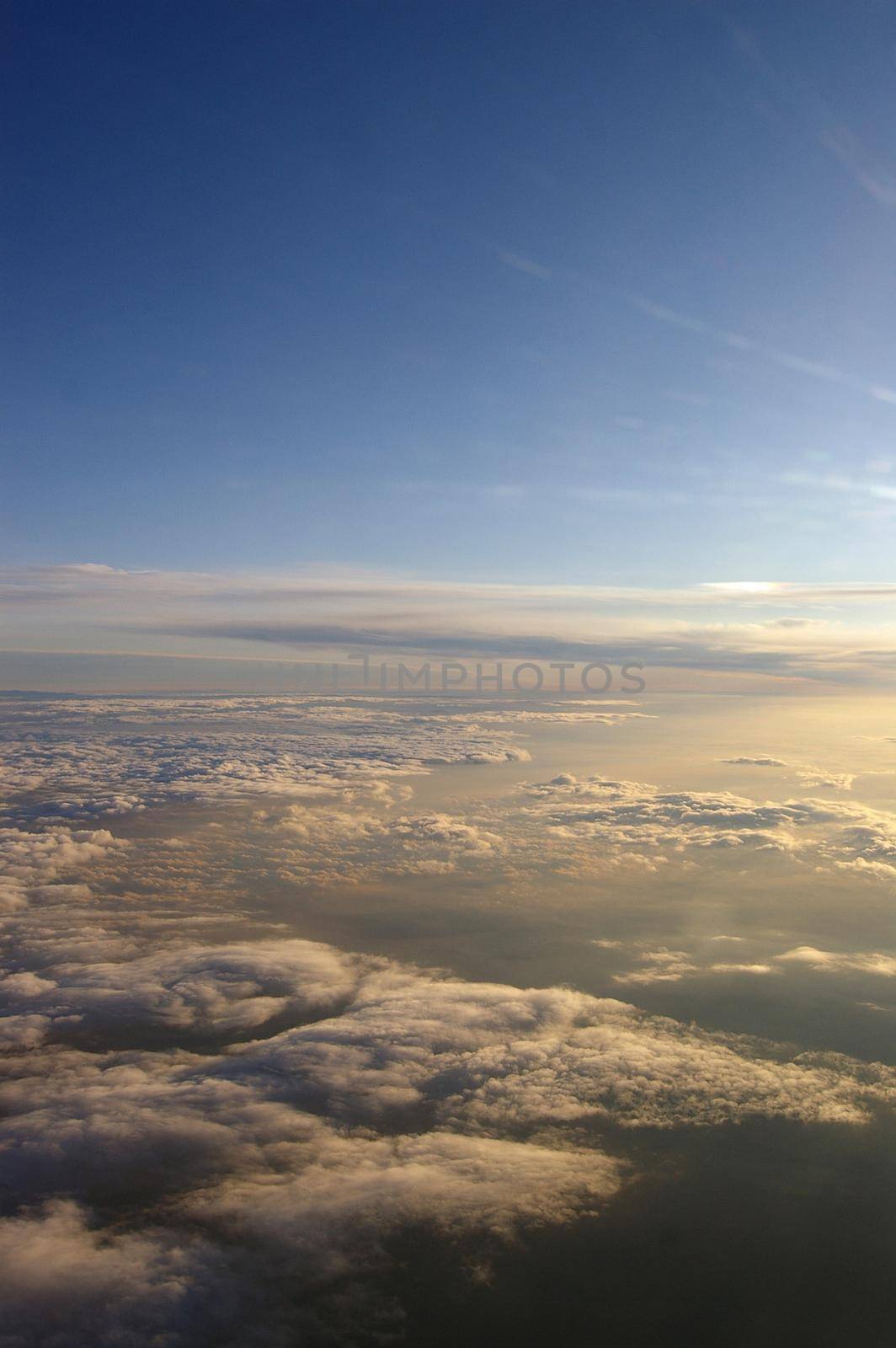 a view of clouds below from a high altitude aircraft as the sun sets
