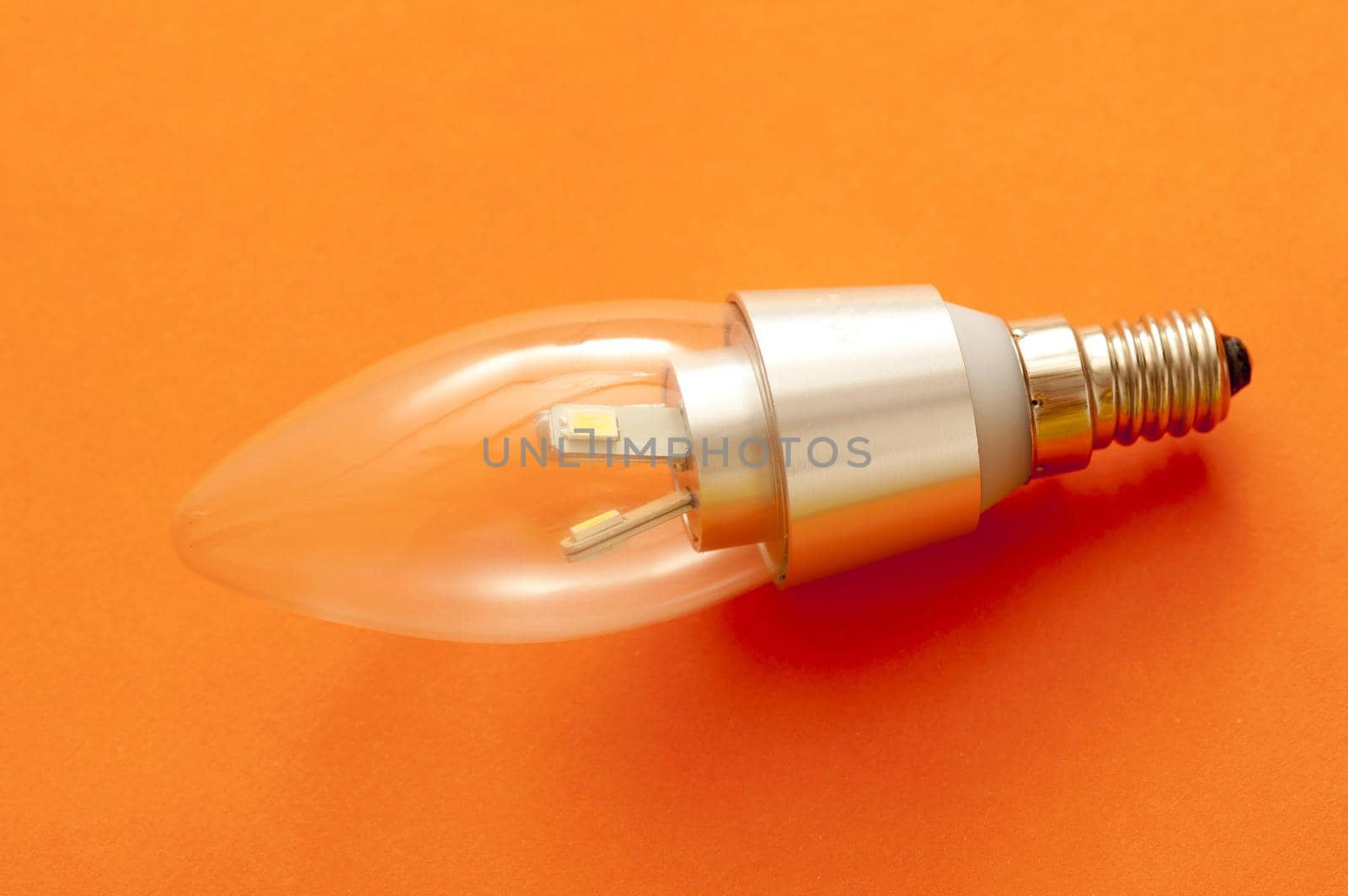 LED candle shaped light bulb with a screw fitting on an orange background showing diode detail