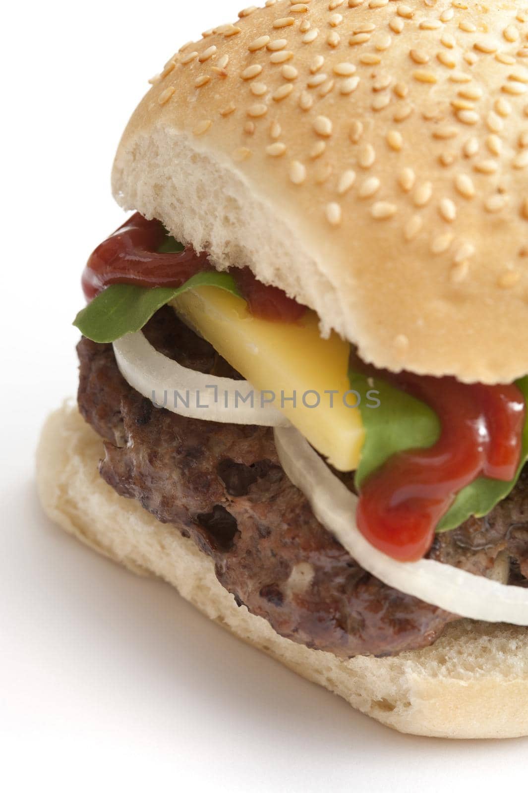 Cropped view of hamburger topped with cheese, lettuce, onion and ketchup with sesame bun over white