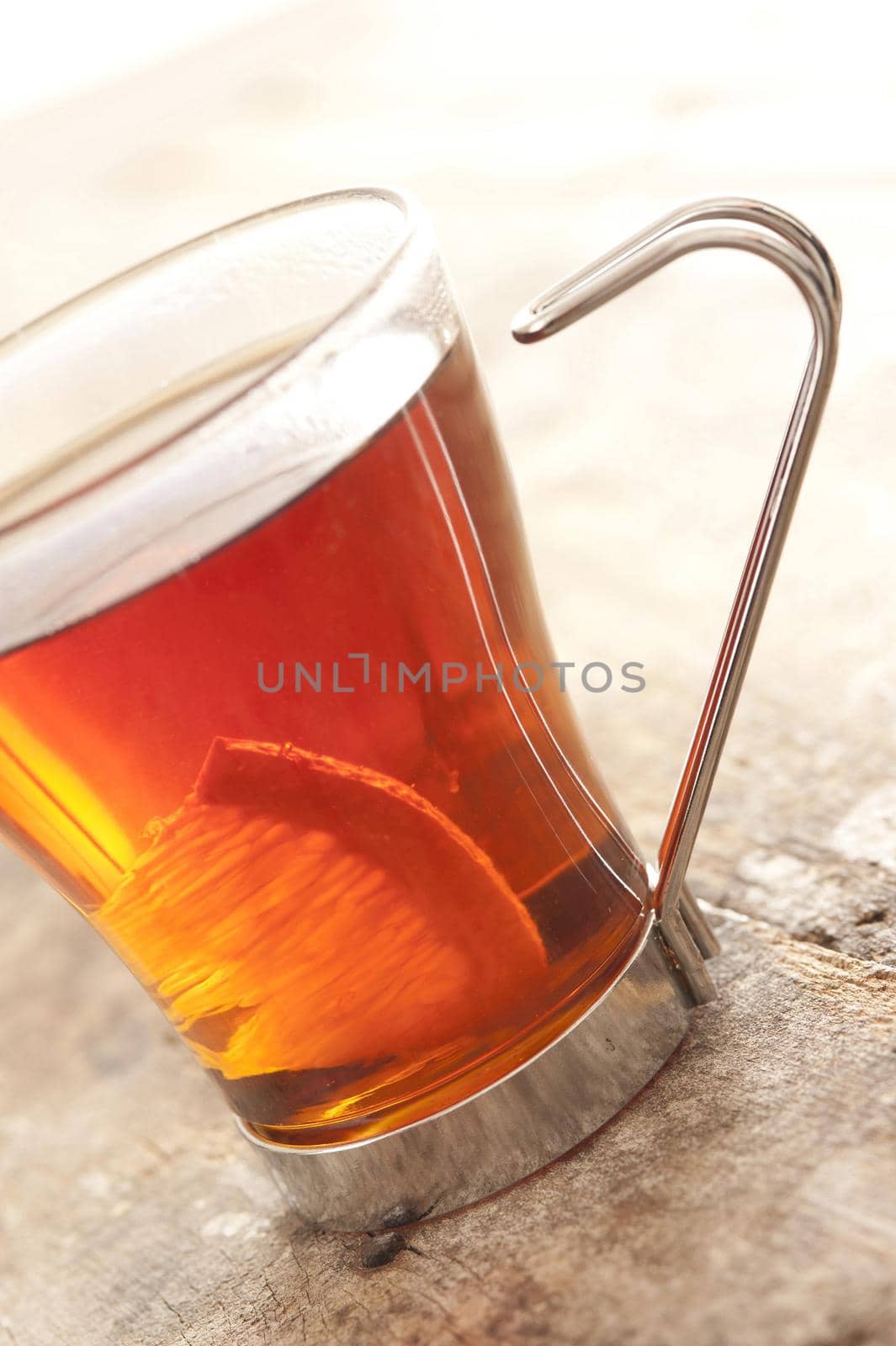 Glass mug of delicious tangy lemon tea with a slice of fresh lemon viewed at a tilted angle on a wooden table