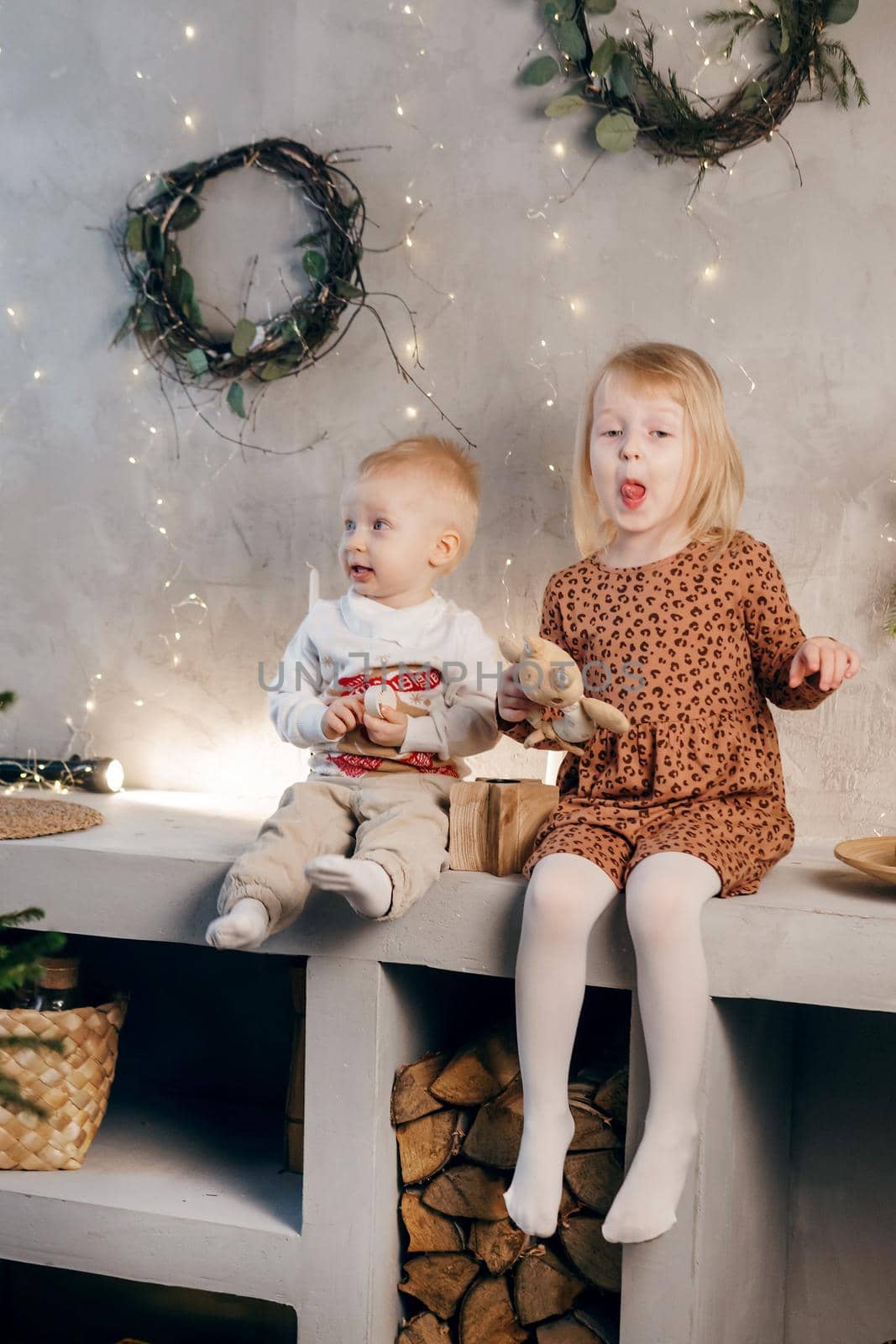 Little brother and sister play on Christmas eve in a beautiful house decorated for the New Year holidays. Children are playing with a Christmas gift. Scandinavian-style interior with live fir trees and a wooden staircase.