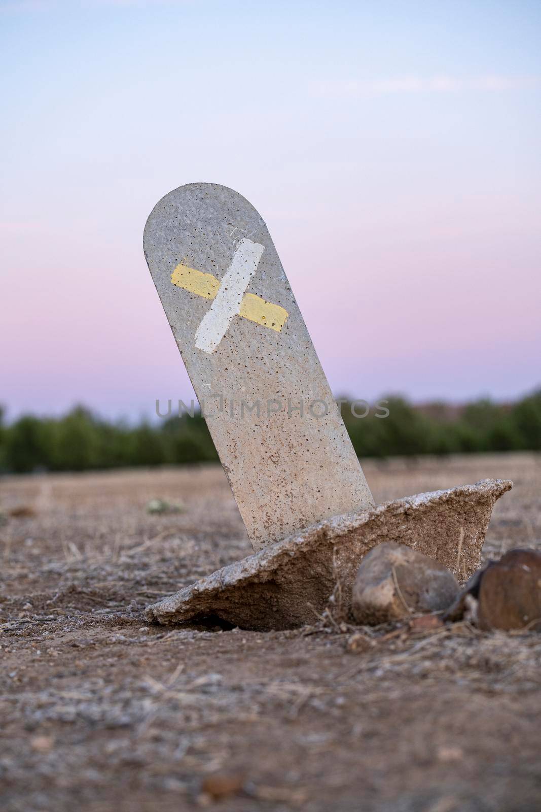 Typical signal trails, marked on a small stone post ripped from the ground in the countryside. Wrong way or direction. Colorful sunset sky in background