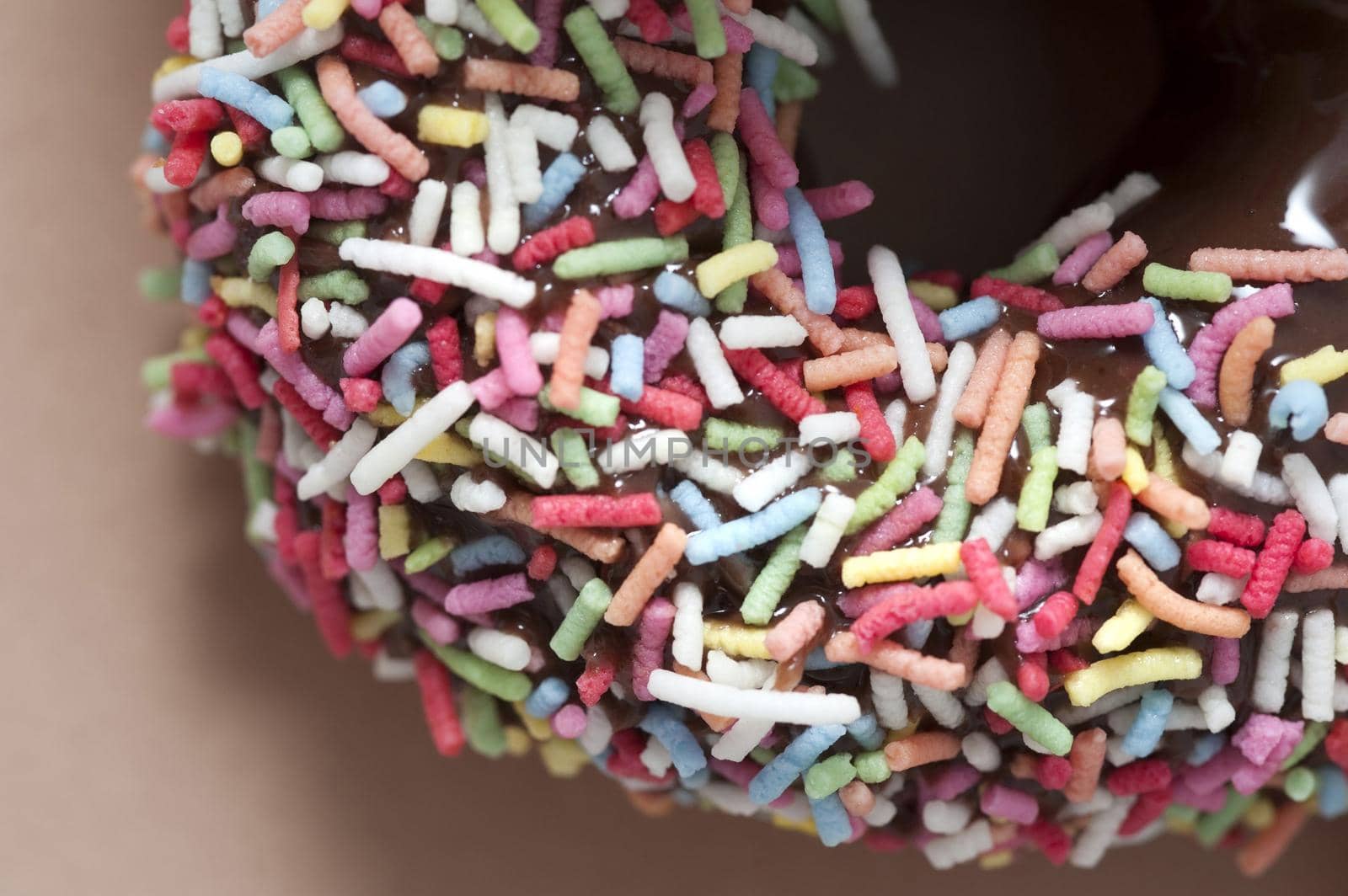 Background texture of a freshly baked decorated chocolate ring doughnut or donut covered in colorful sprinkles