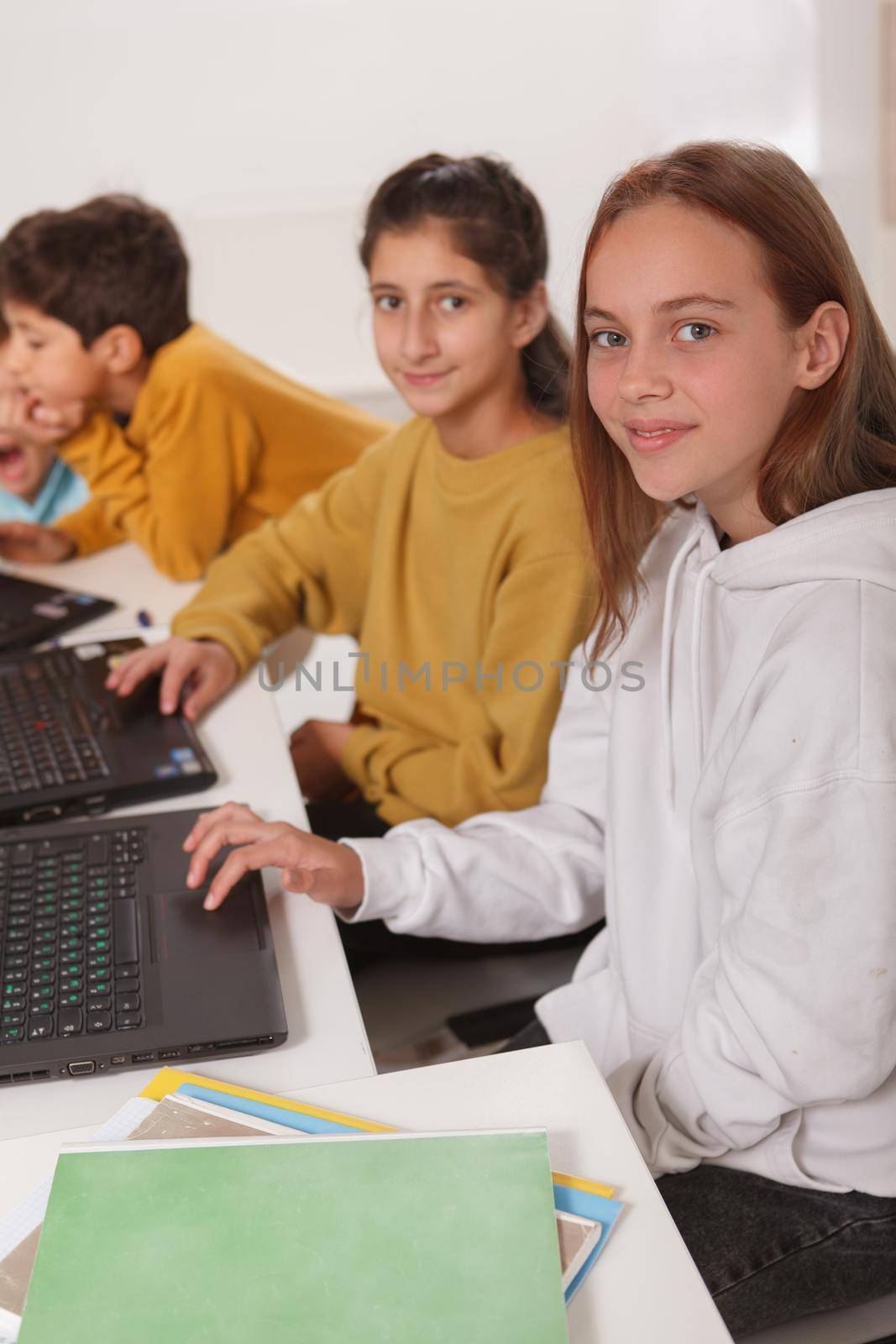 Vertical shot of teen girls students smiling to the camera while working on computers at school