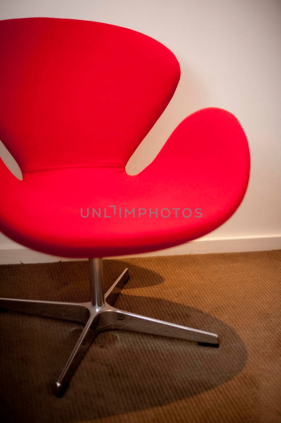 Close up of a modern red arm chair with a modular design and steel base on a brown carpet
