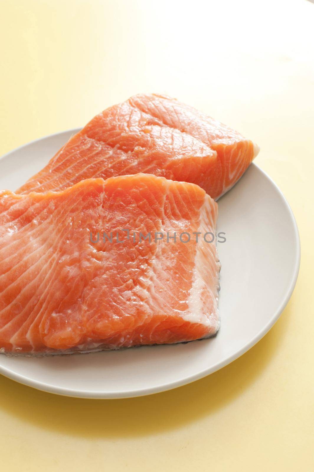 Close up Raw Salmon Fish Meat Slices on a White Plate, Placed on a Yellow Table.