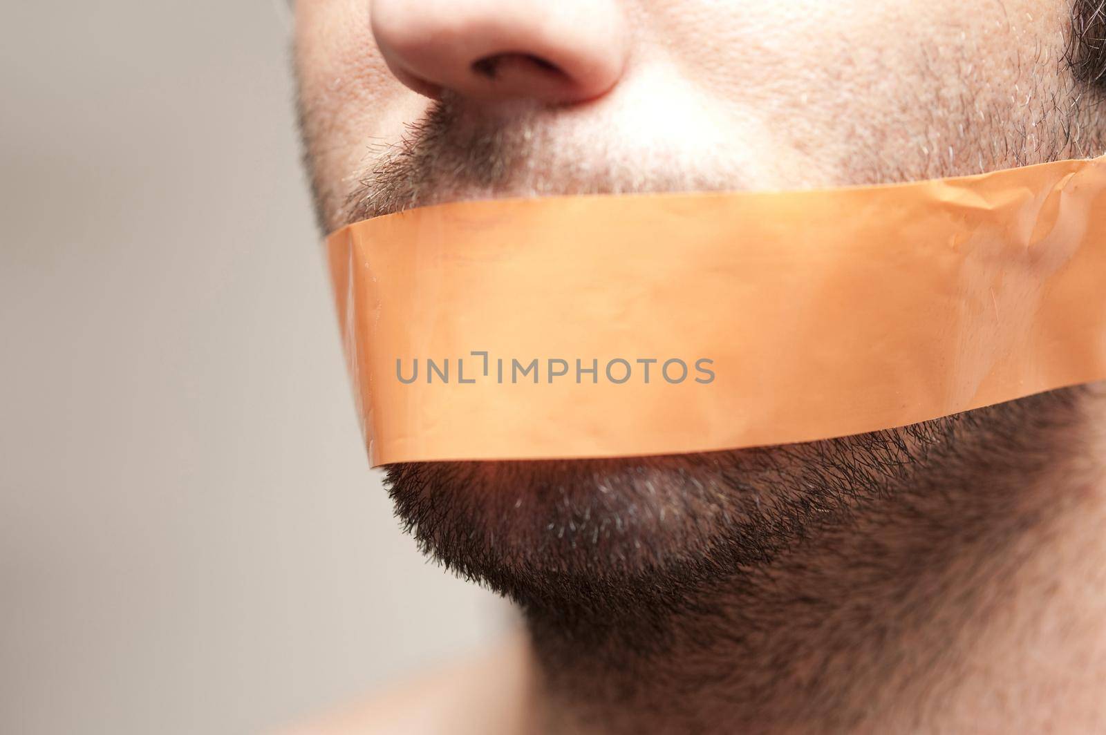 Can't Speak - Close Up of Man with Facial Hair Stubble Gagged with Orange Tape Across Mouth