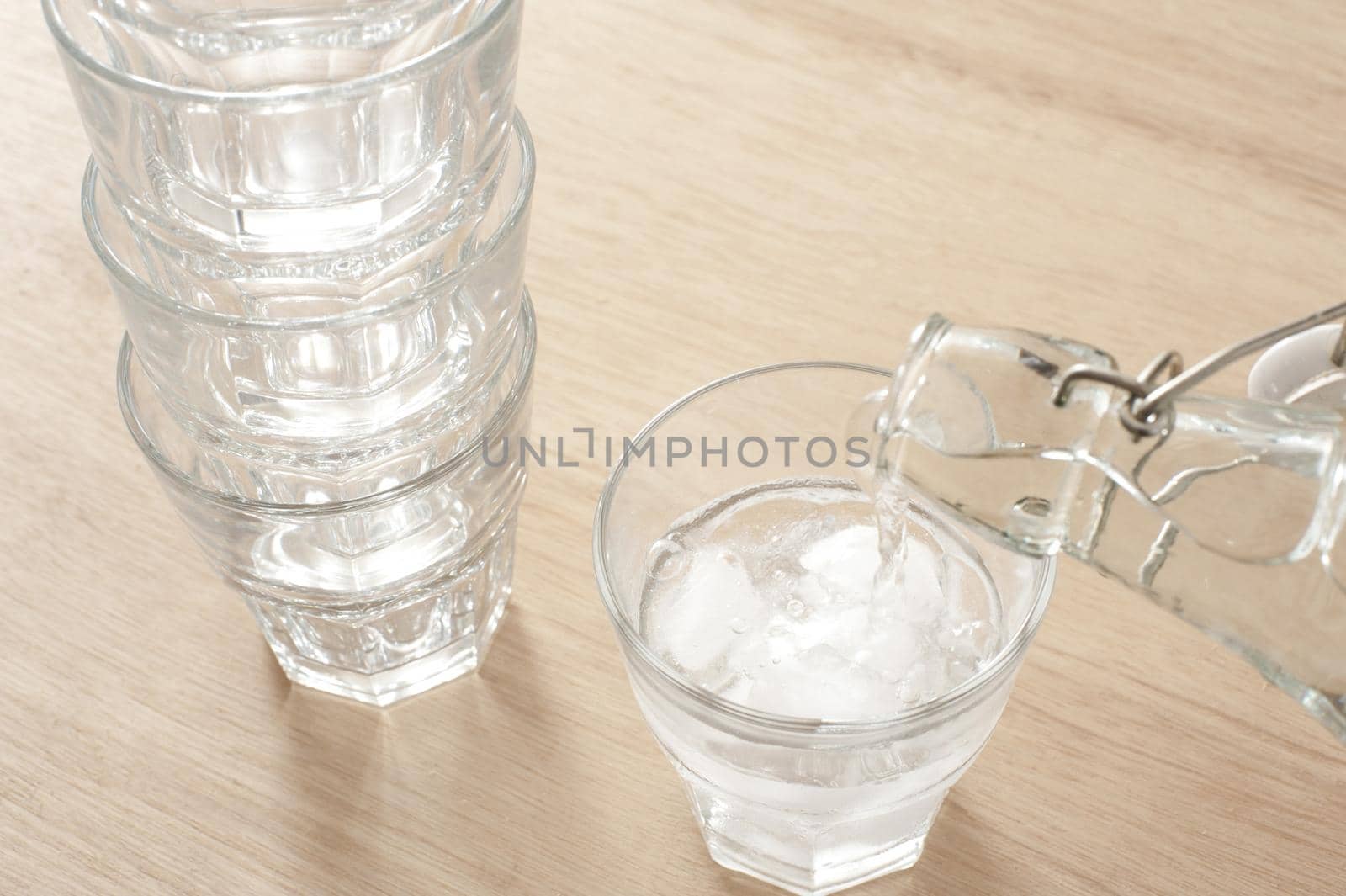 Pouring a glass of fresh pure water from a glass bottle into a tumbler containing ice for a healthy refreshing drink