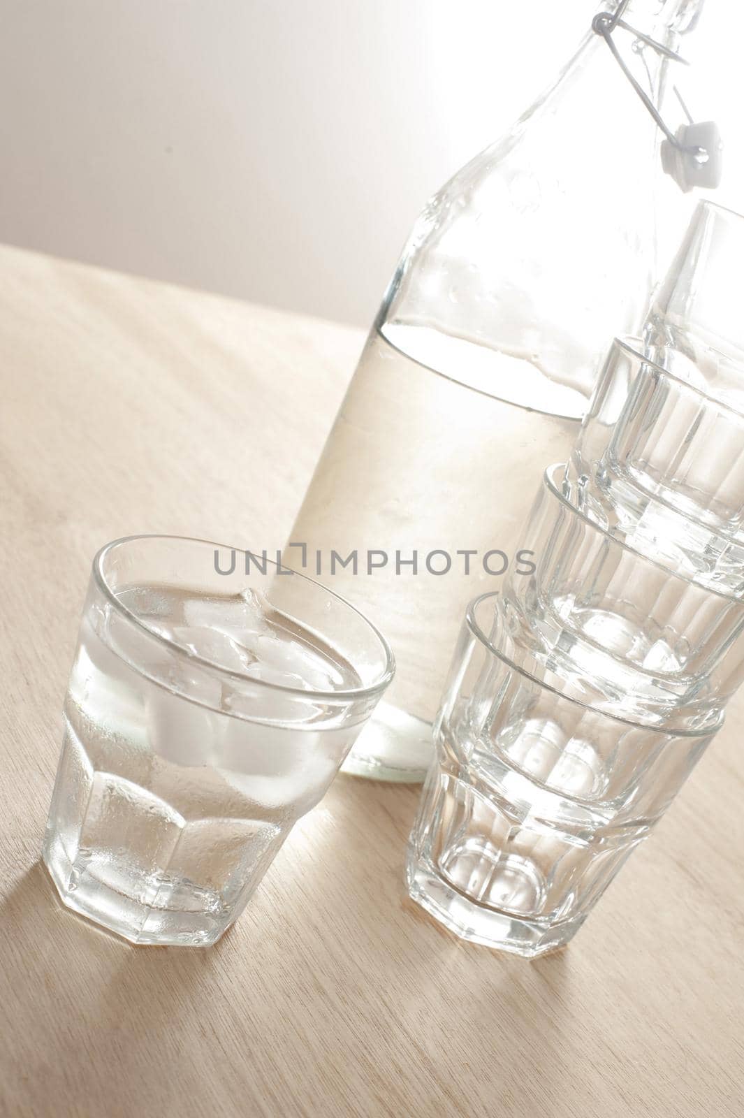 Glass of ice cold water in a tumbler with a reusable glass bottle from the refrigerator full of healthy pure water with additional empty glasses alongside
