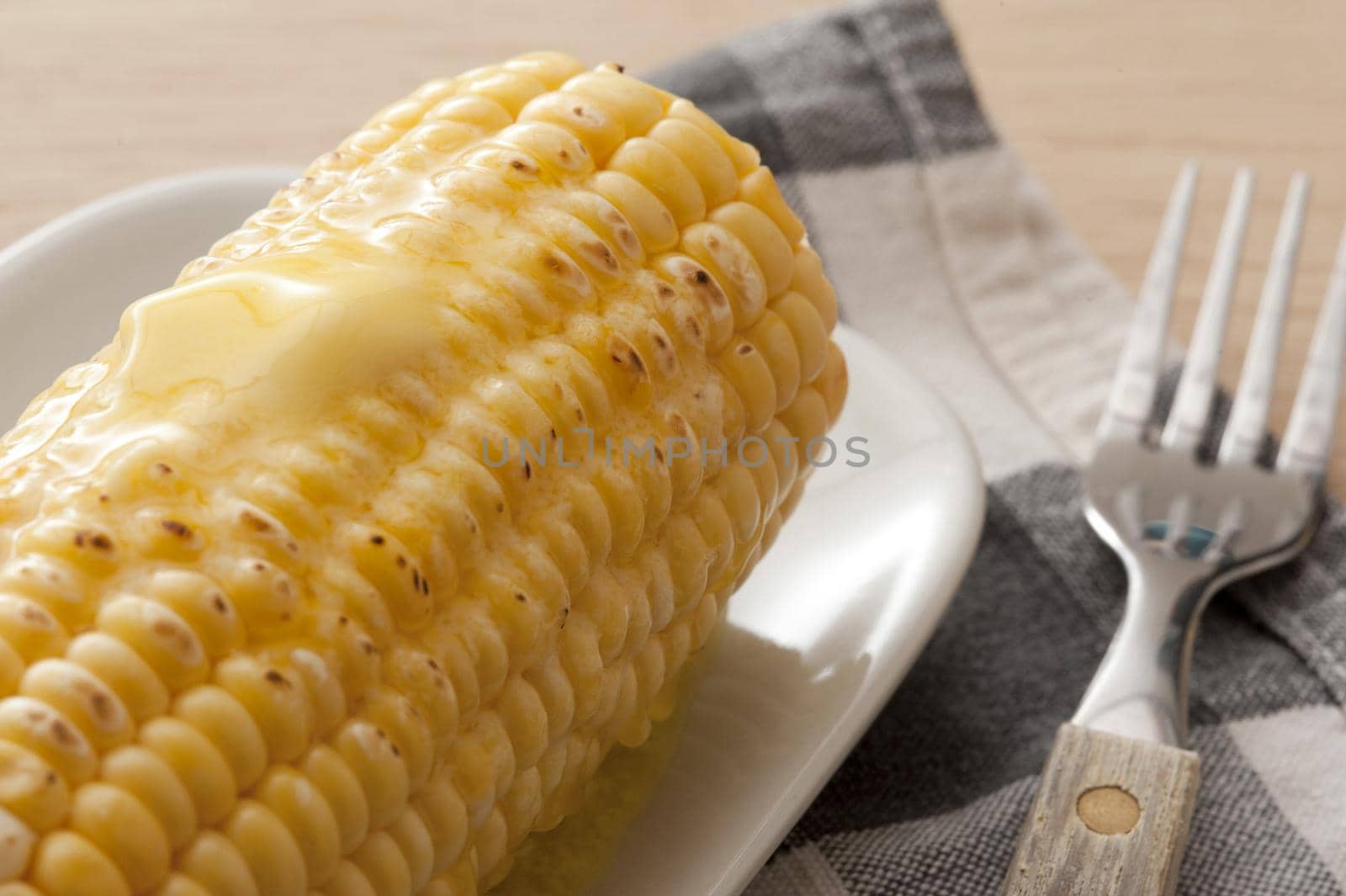 Close-up of cooked corn-cob with butter on top lying on plate with fork