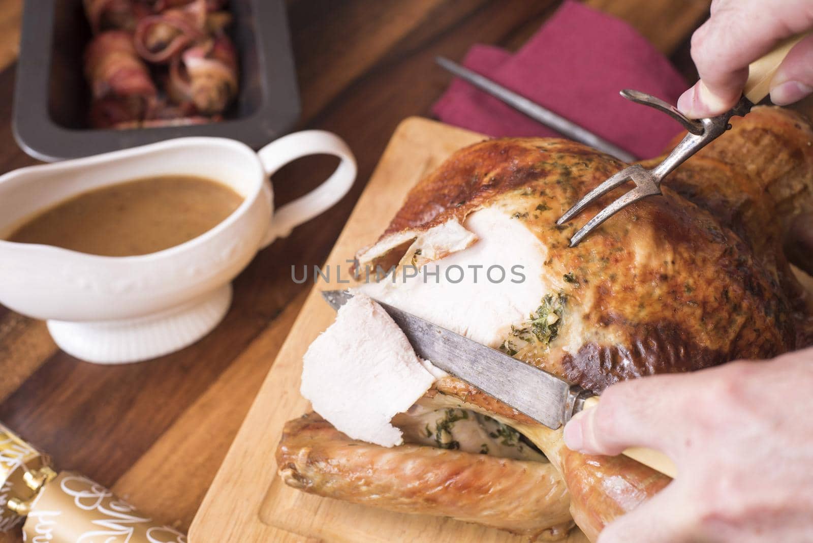 Man carving the Christmas turkey with a carving knife and fork at the table with a gravy sauce boat and roast potatoes alongside