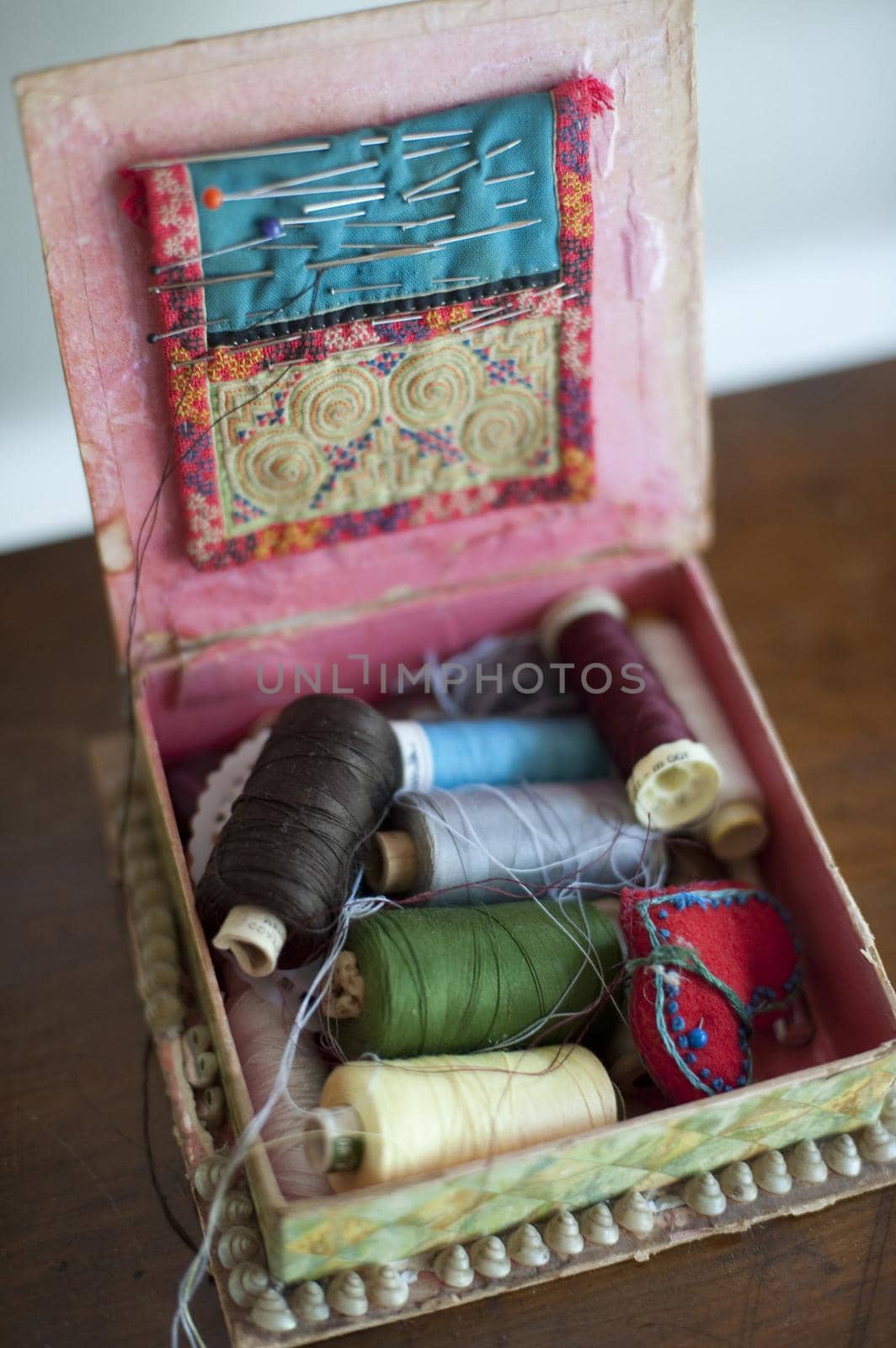 Open sewing box with reels of colorful thread and needles and pins in a cushion in the lid in a high angle view