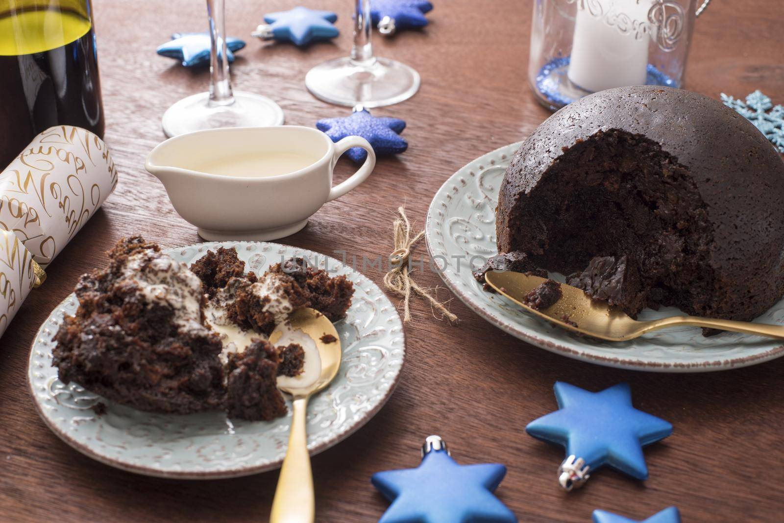 Serving of homemade fruity Christmas pudding topped with brandy cream on a festive dinner table with blue themed decorations