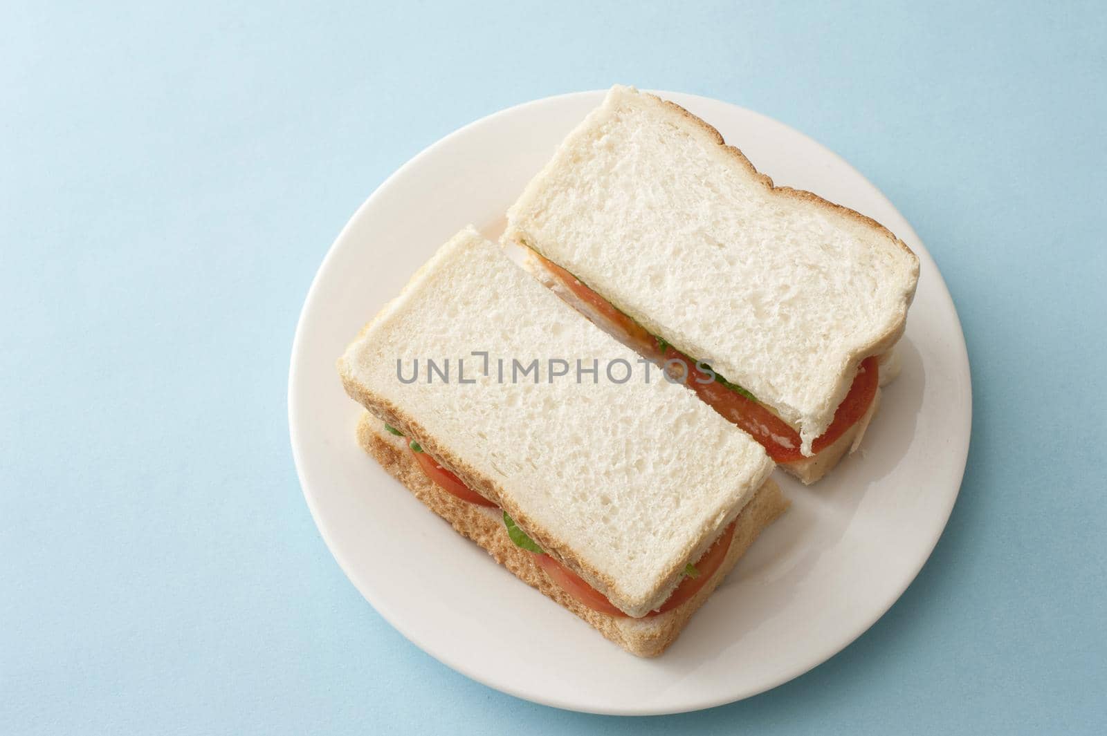 View from above on two slices of a white bread sandwich on round plate with copy space over blue table