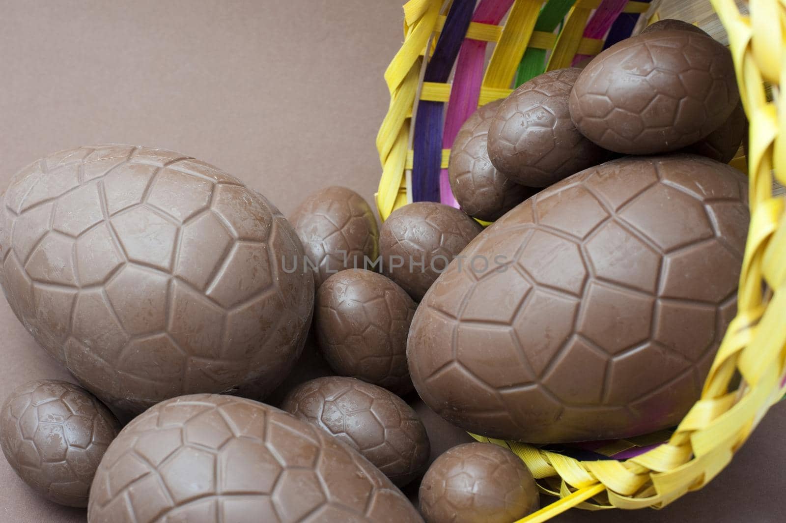 Assorted sized chocolate Easter eggs spilling out of a decorative wicker basket