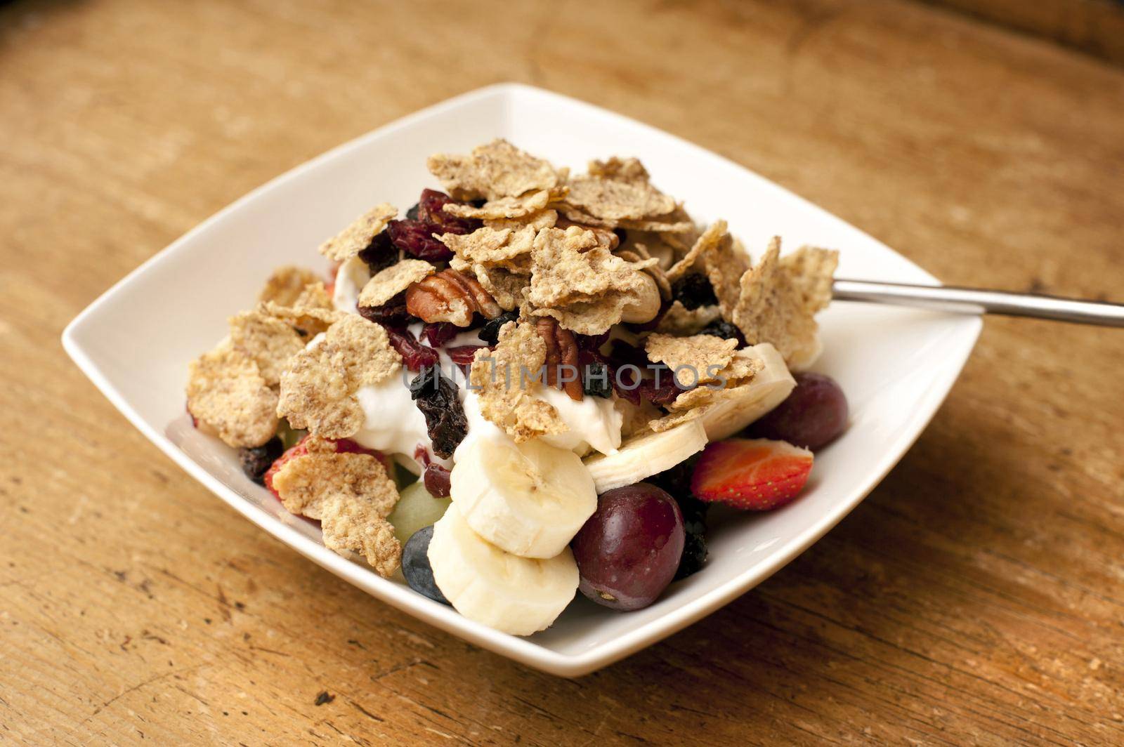 Muesli with fresh diced fruit including berries and banana served in a bowl for breakfast with a dollop of fresh plain yogurt