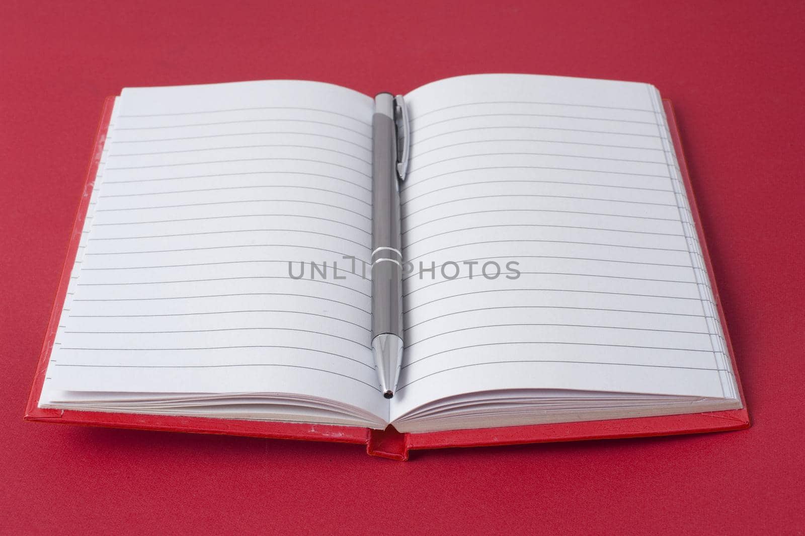 Red notebook and ball pen on red background