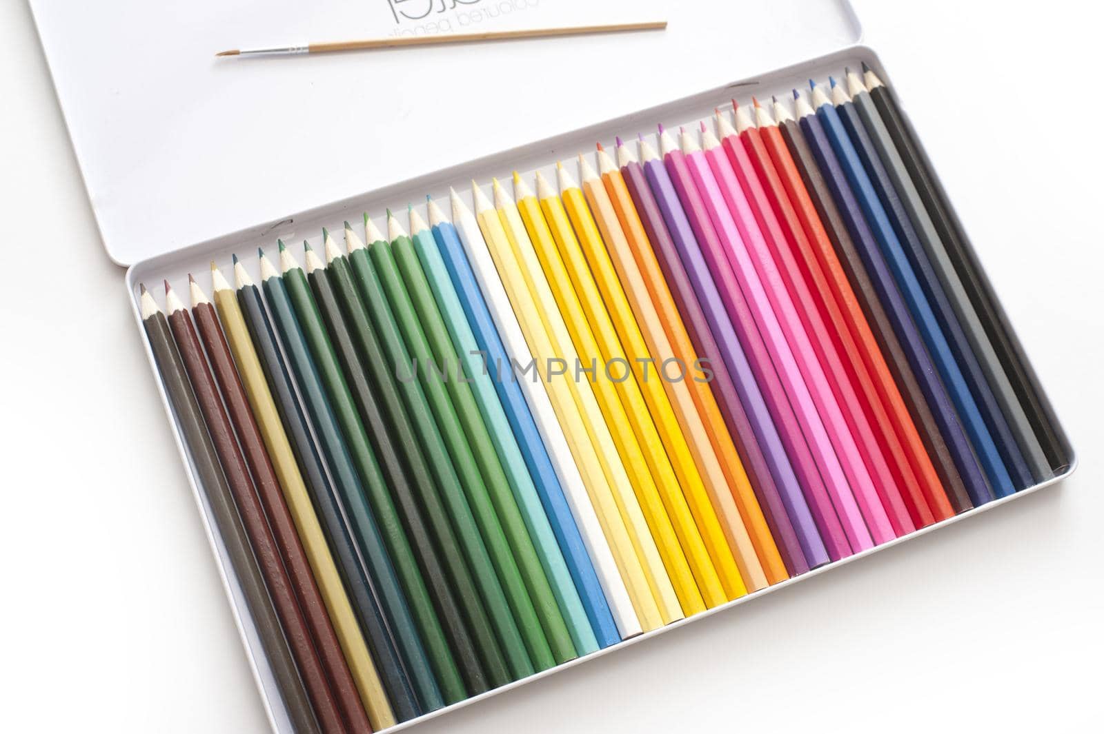 Close up of open case full of various colored pencils and single brush in lid over white background