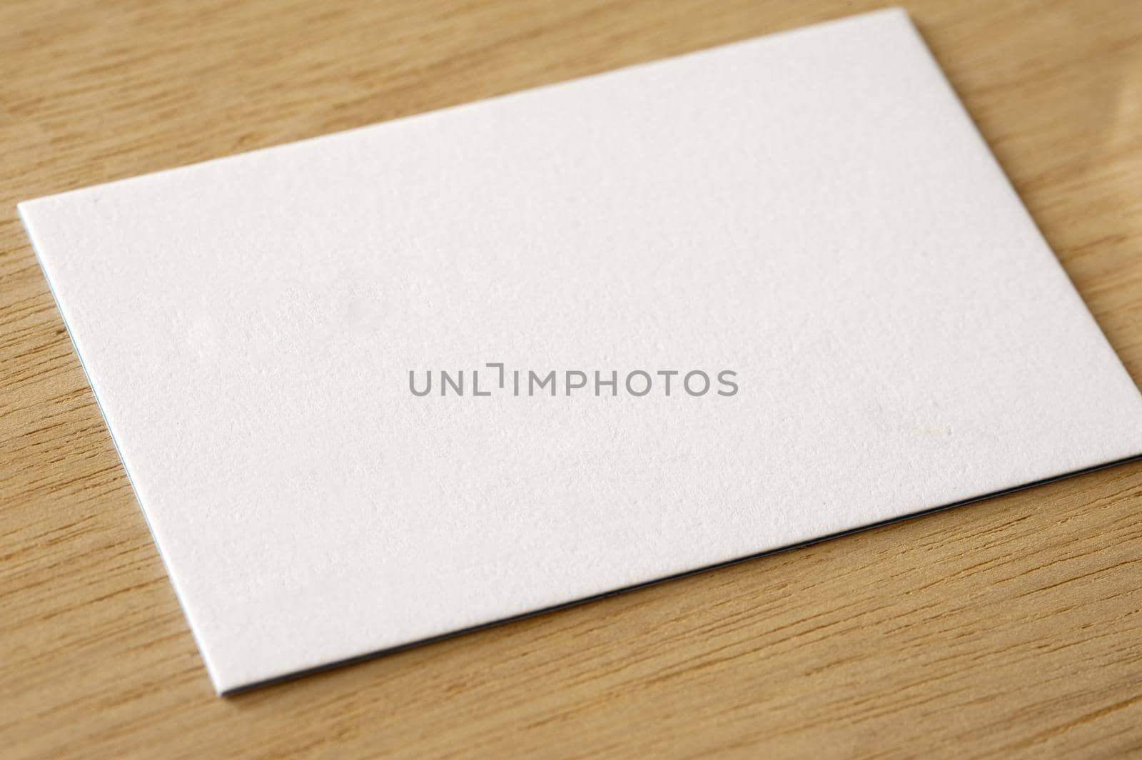 Plain white textured card on a wooden desk with copy space for your text viewed at an oblique angle