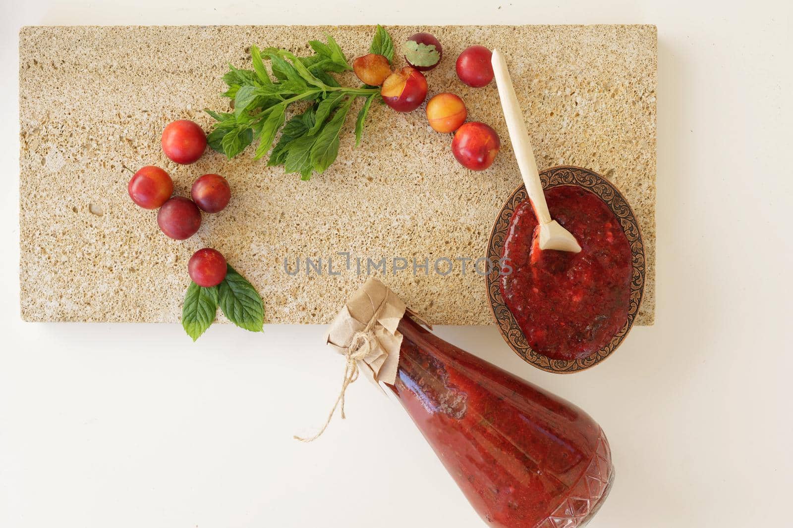 Georgian tkemali sauce in a glass bottle with ingredients on natural stone background