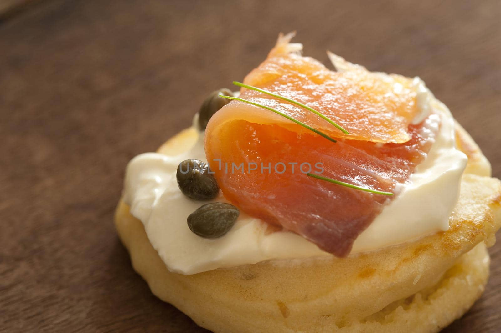 Gourmet appetizer with smoked salmon, capers and cream cheese served on a blini on a wooden table