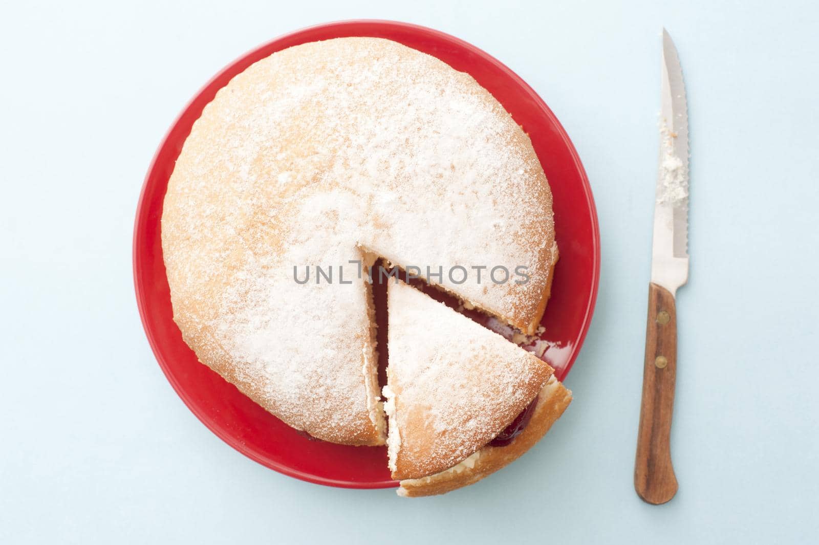 Top down view recently sliced wedge of delicious cake over round red plate next to cutting knife over table
