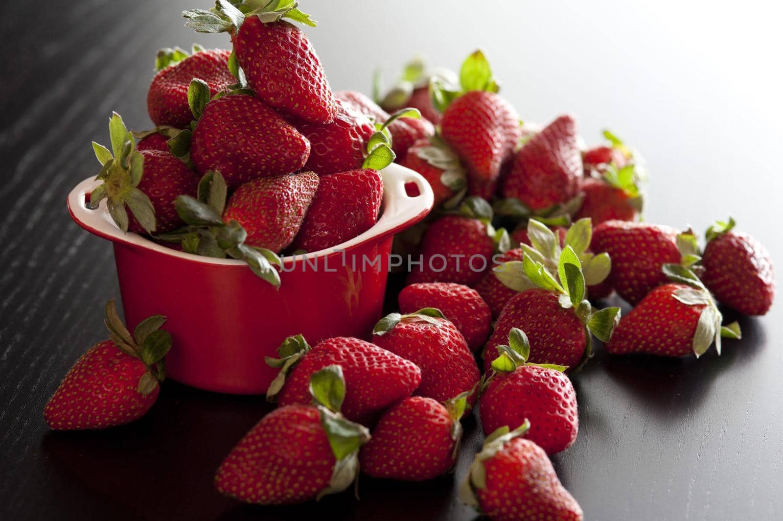 Fresh juicy ripe red strawberries overflowing from a small red ceramic ramekin ready for a tasty vegetarian snack or delicious dessert