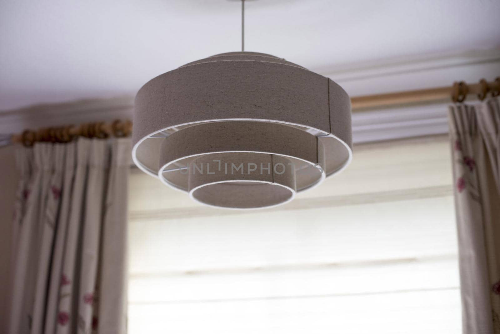A white, contemporary ceiling light shade hanging from the interior of a modern home with hanging curtains.