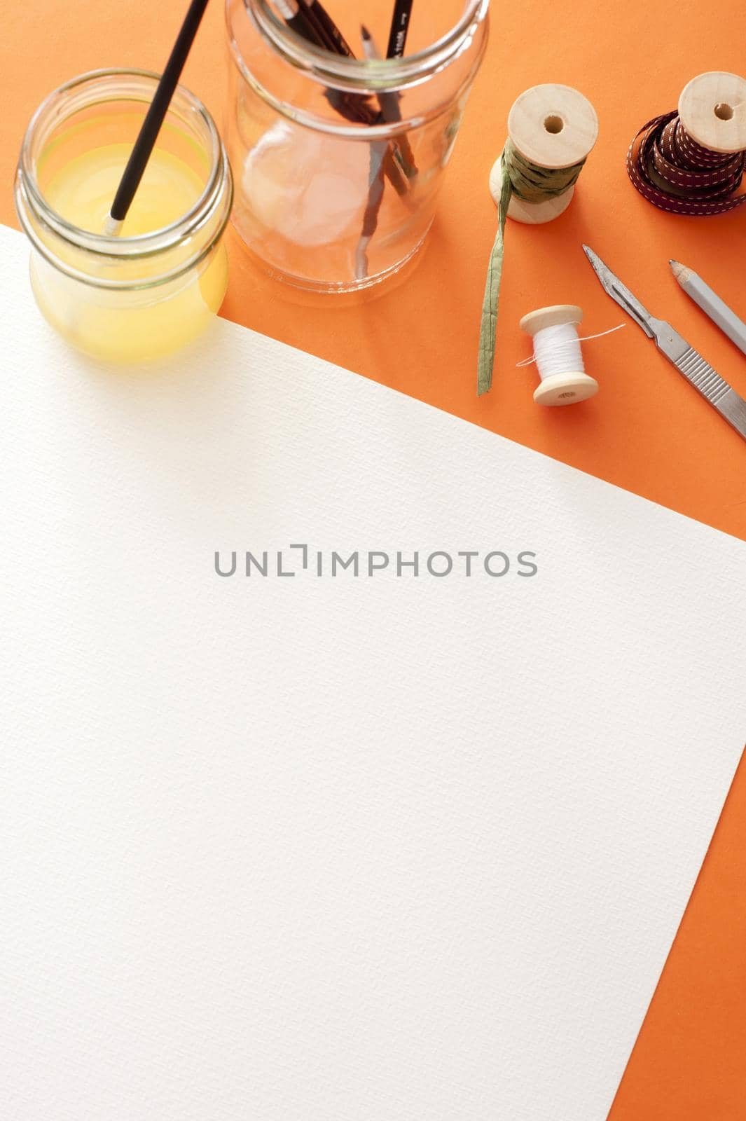 Blank white canvas paper with copy space under spools, knife, brushes and paint on the top edge