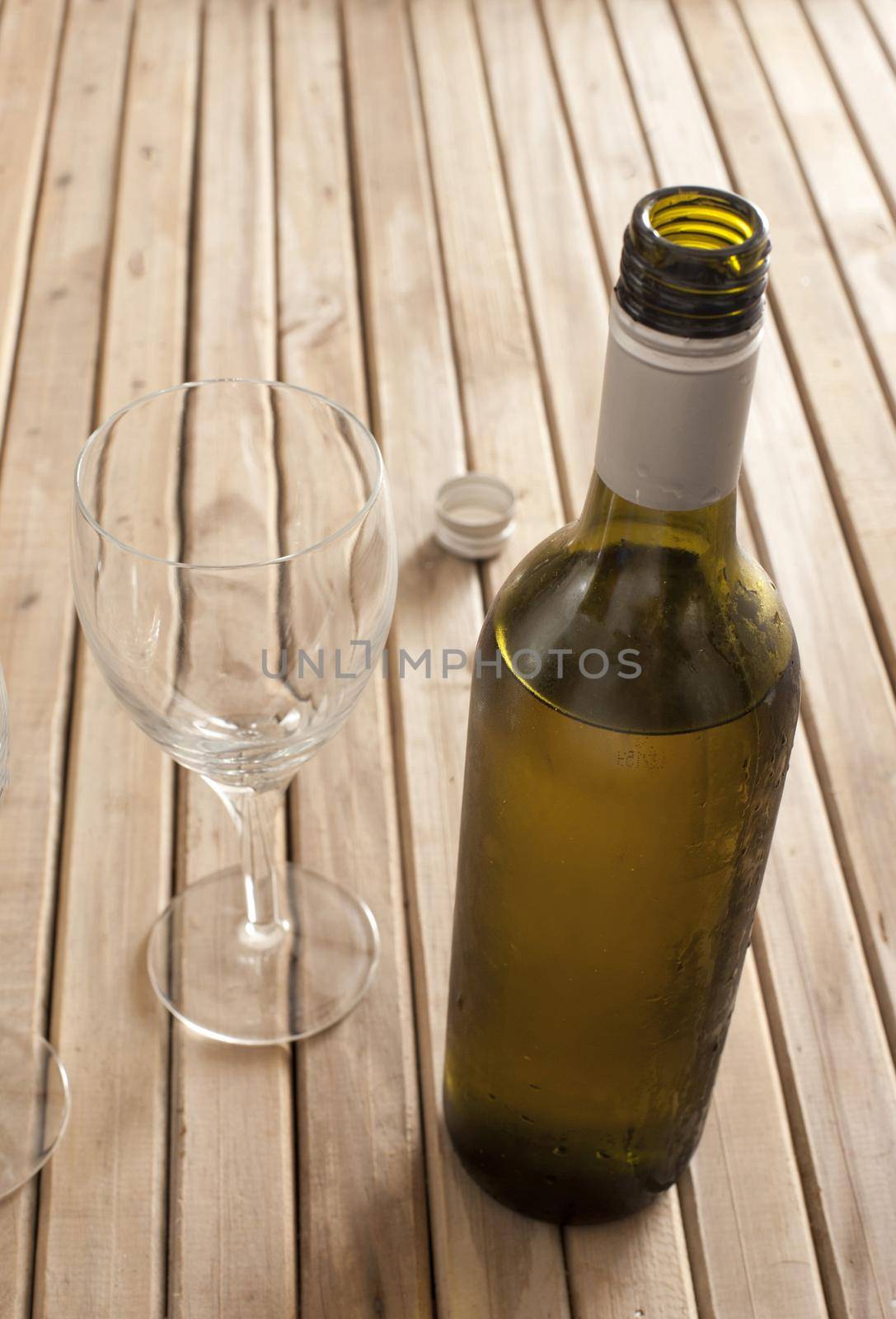 Opened unlabelled bottle of white wine left standing to breath standing on a wooden table with two empty wine glasses, with copyspace