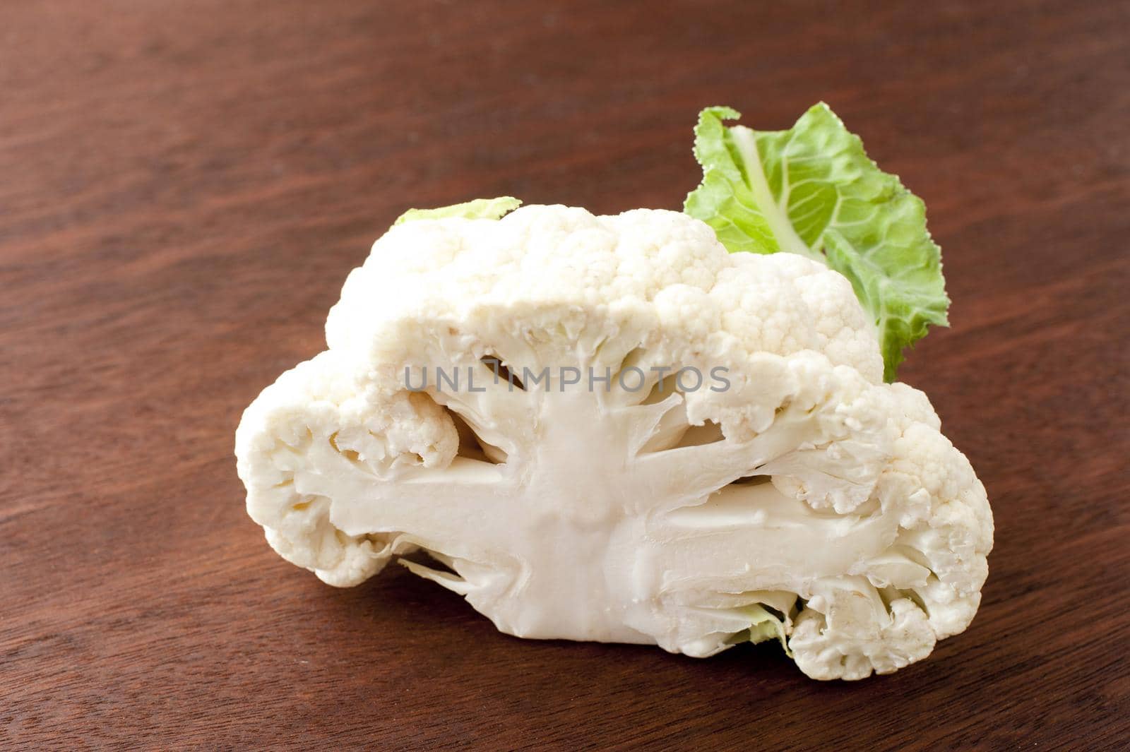 Sliced through head of fresh white cauliflower on a wooden chopping board viewed with focus to the cross-section