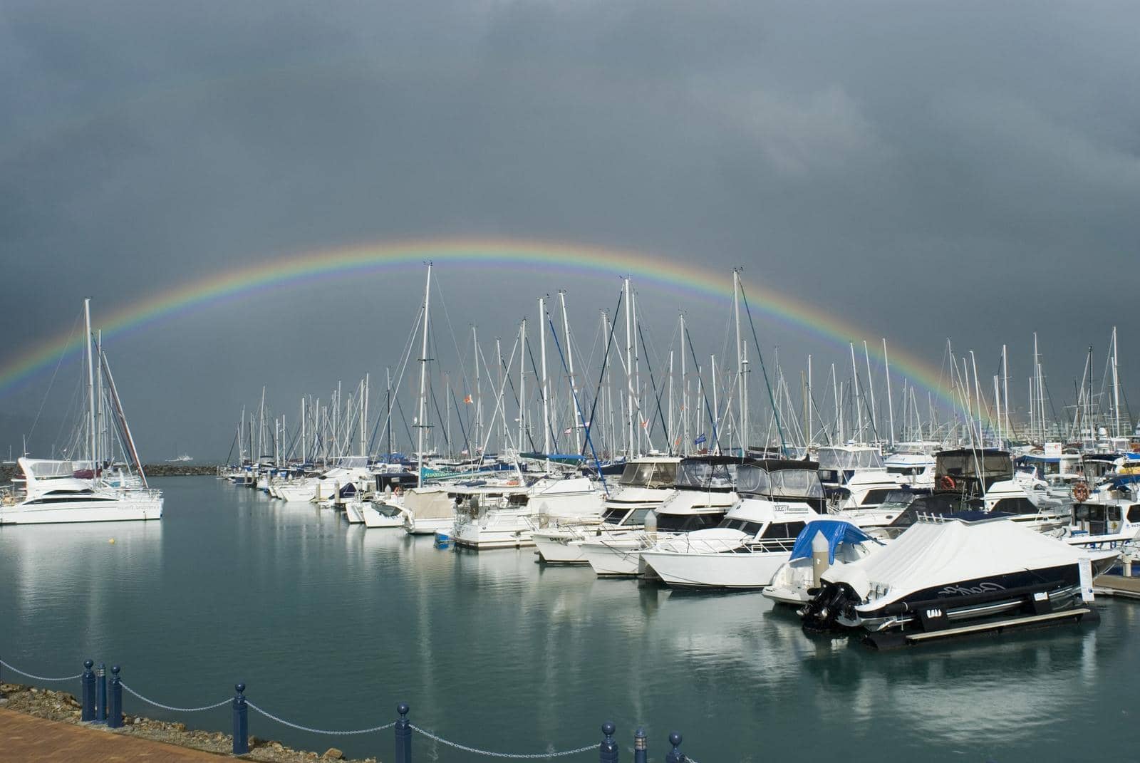 a rainbow and dark storm clouds over yachts in a marina