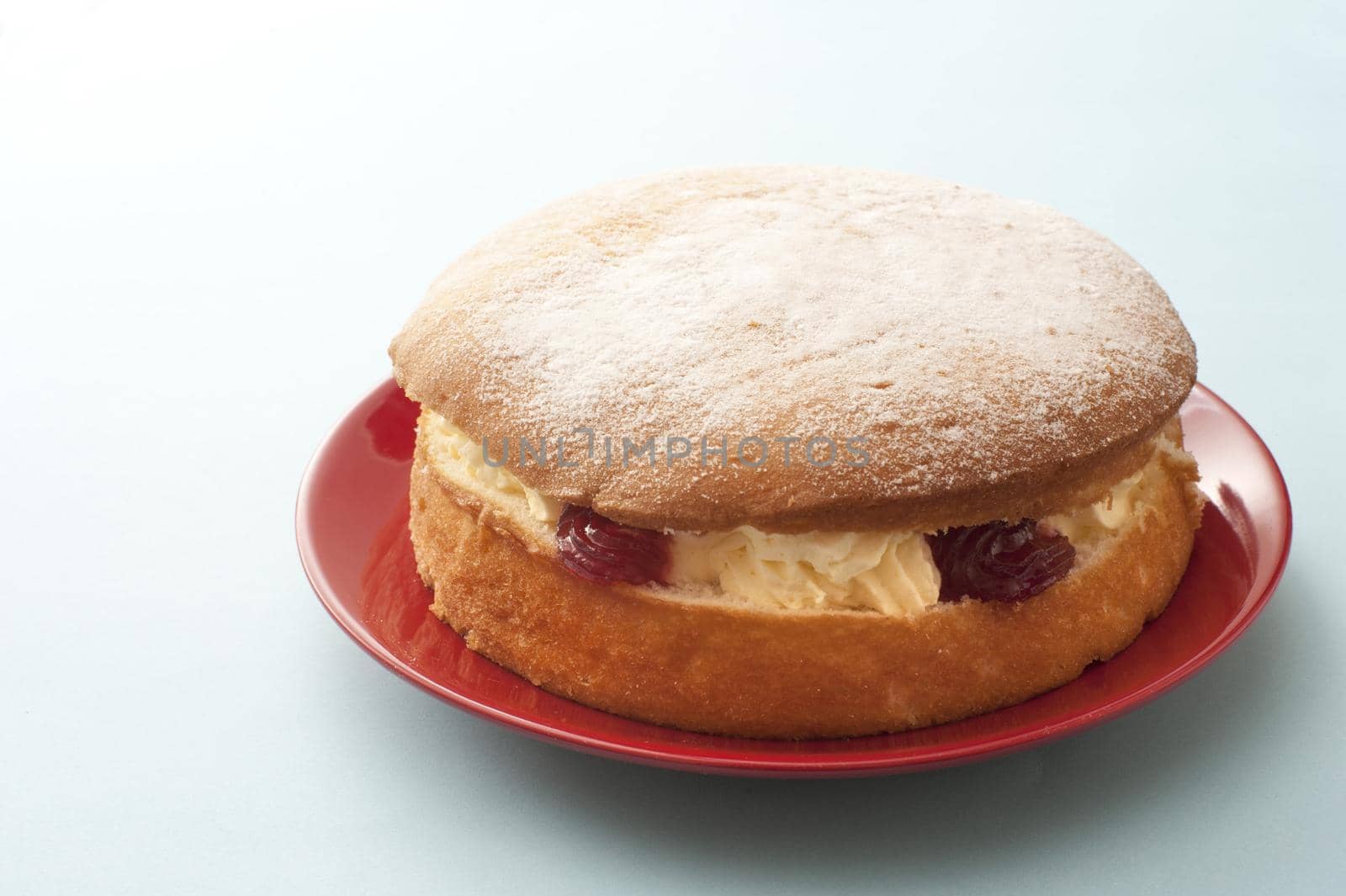 Delicious single little round victoria sandwich sponge cake filled with cream and fruit on red plate over white table