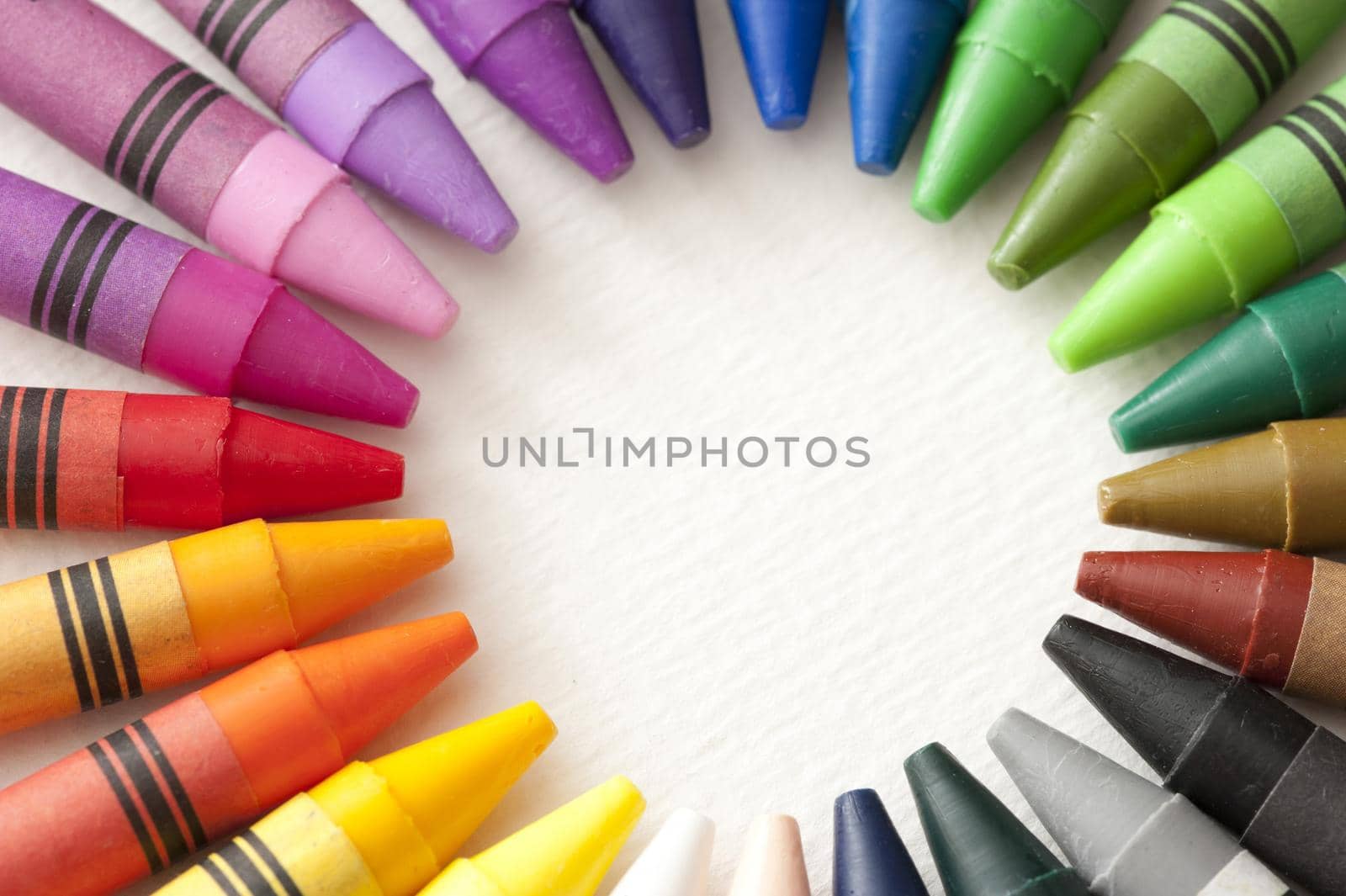 Frame of colorful wax crayons with their points facing inwards in a radiating circle with central blank white copy space