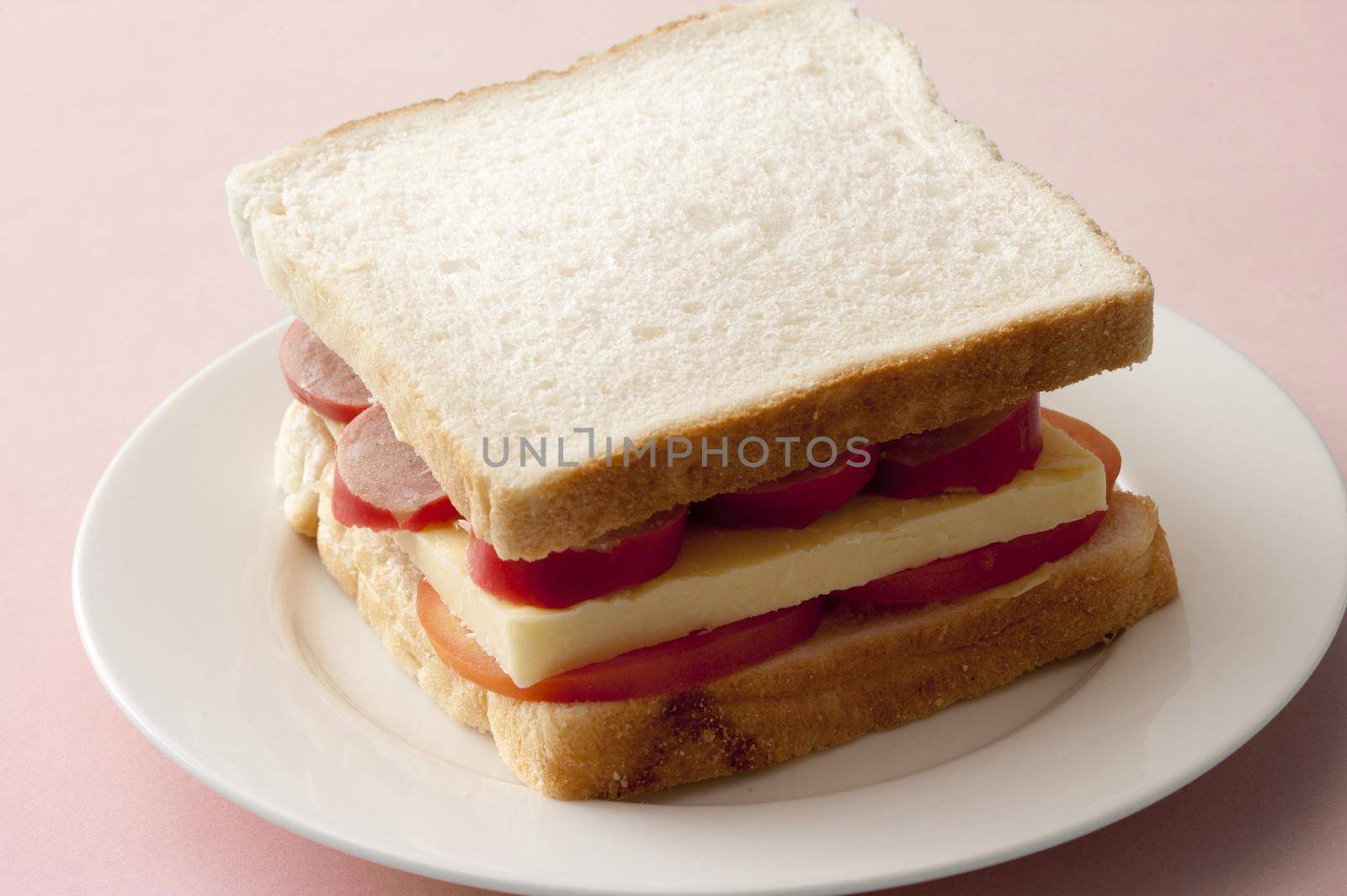 Thick serving of cheese, pepperoni sausage and tomato slices in between two pieces of white bread for delicious sandwich
