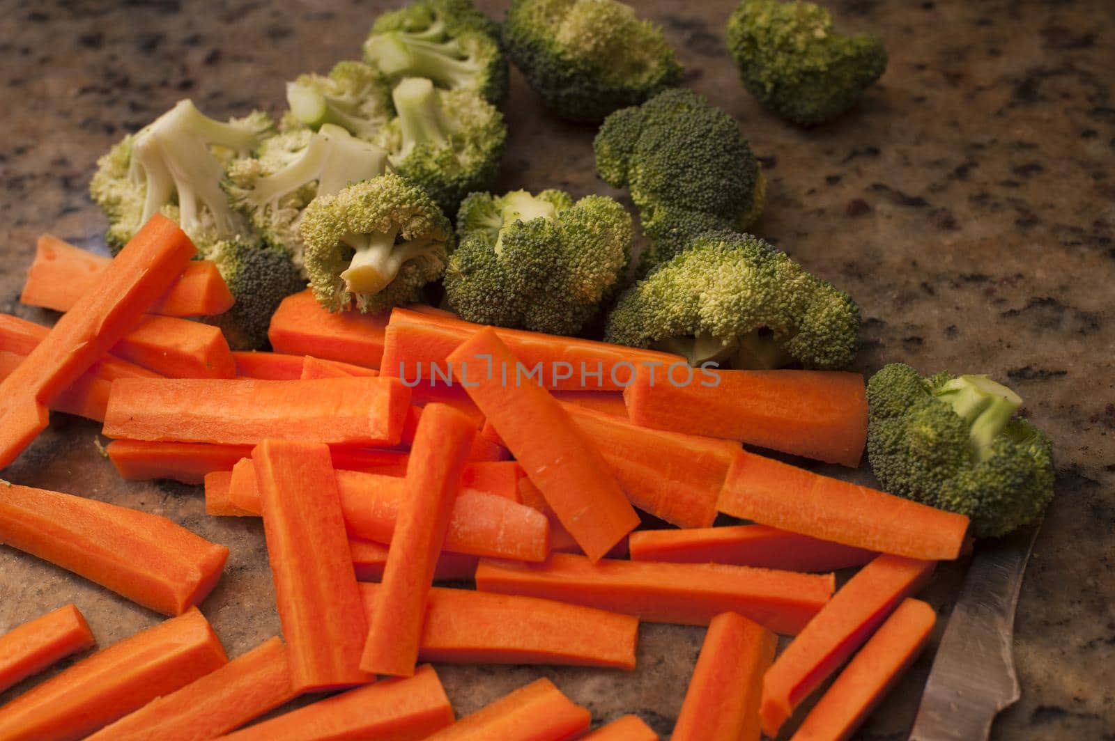 Chopped vegetables on a kitchen counter including carrot batons and broccoli pieces ready to be cooked as accompaniments to a meal