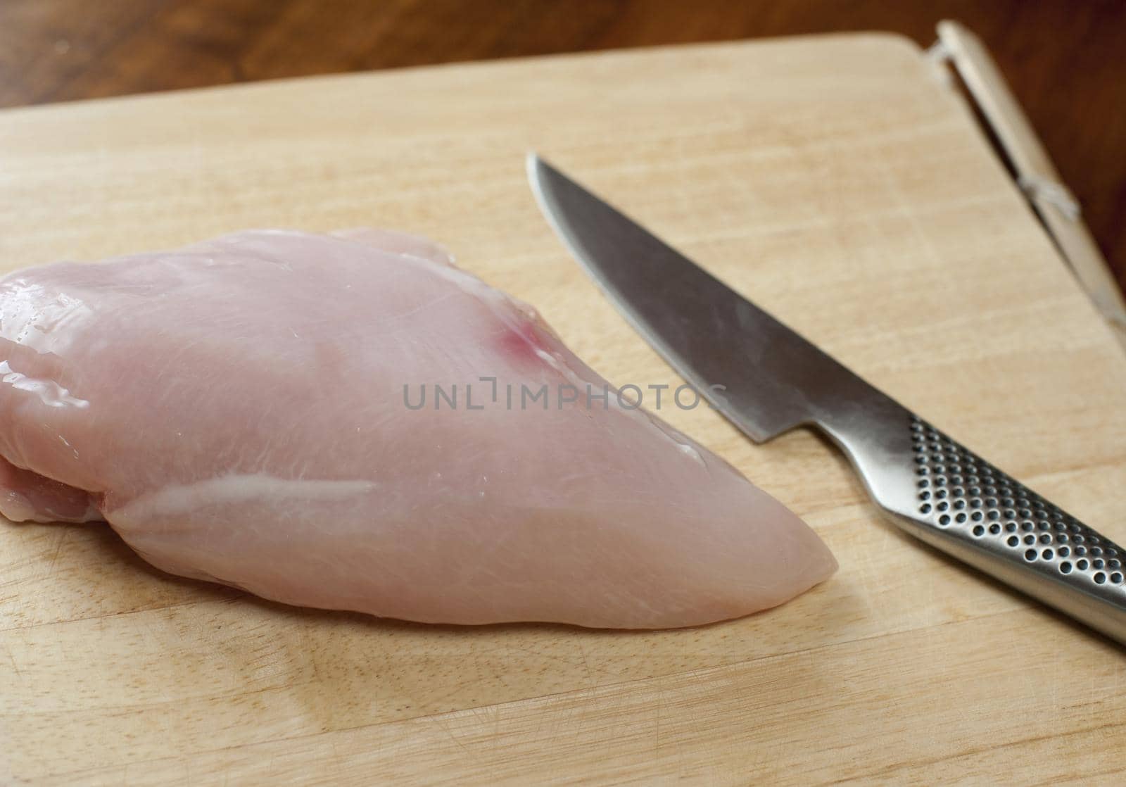 Uncooked lean healthy chicken breast on a wooden chopping board with a sharp kitchen knife , close up view