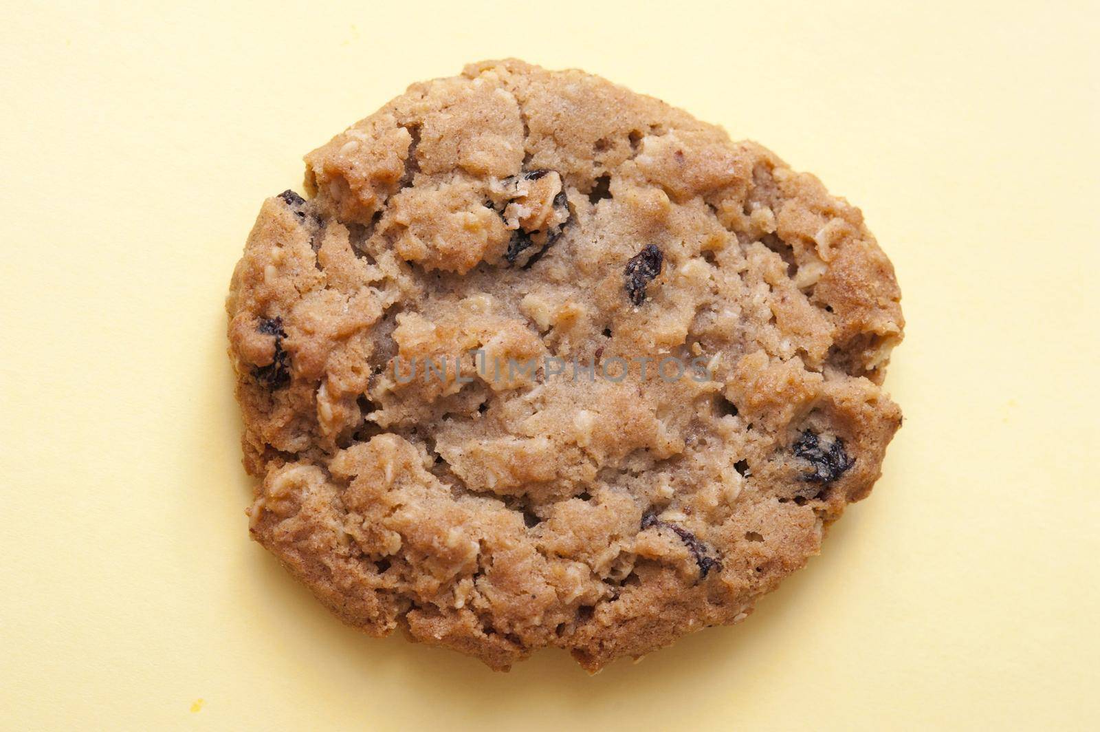 Single round crunchy raisin cookie made with oats on a yellow background, high angle view